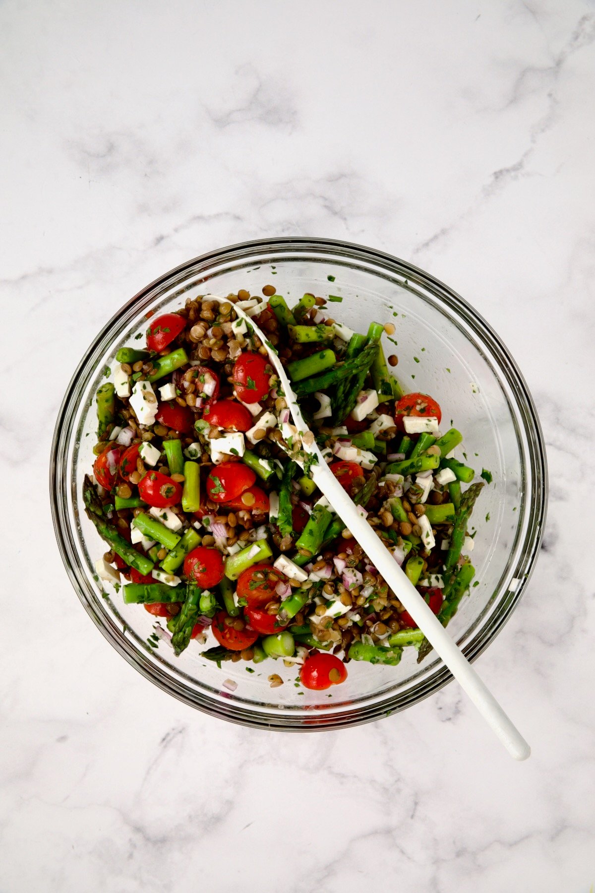 Ingredients for Lemony Lentil Salad with Asparagus and Tomatoes in glass bowl after being combined with feta cheese added.