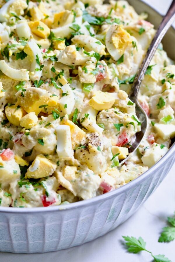 Potato Salad with Horseradish Dressing in light blue bowl with serving spoon garnished with parsley.