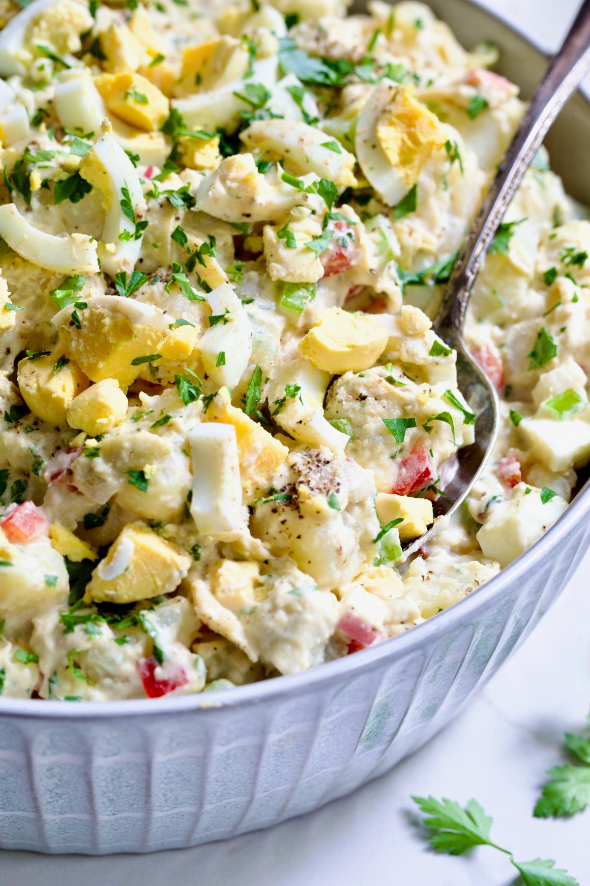 Potato Salad with Horseradish Dressing in light blue bowl with serving spoon garnished with parsley.