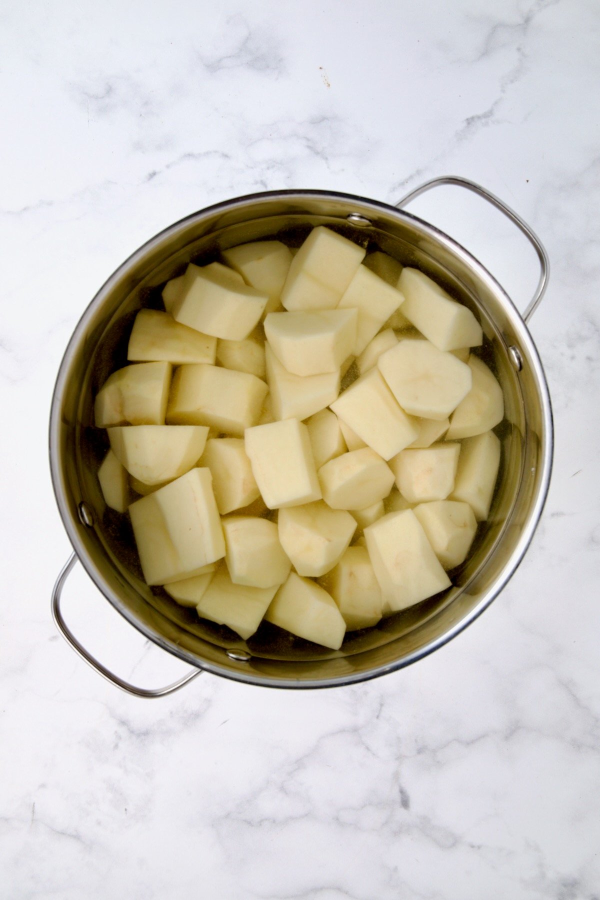 Uncooked peeled potatoes in water in stainless steel pot.