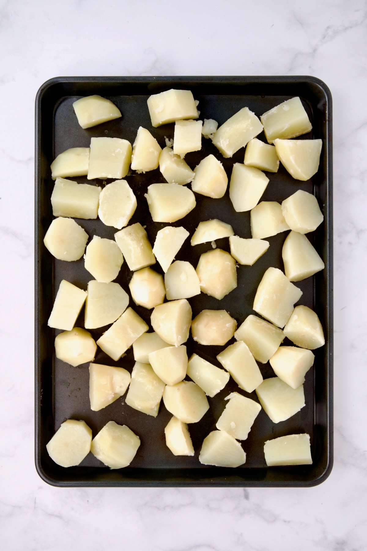 Cooked cubed potatoes on rimmed sheet pan.
