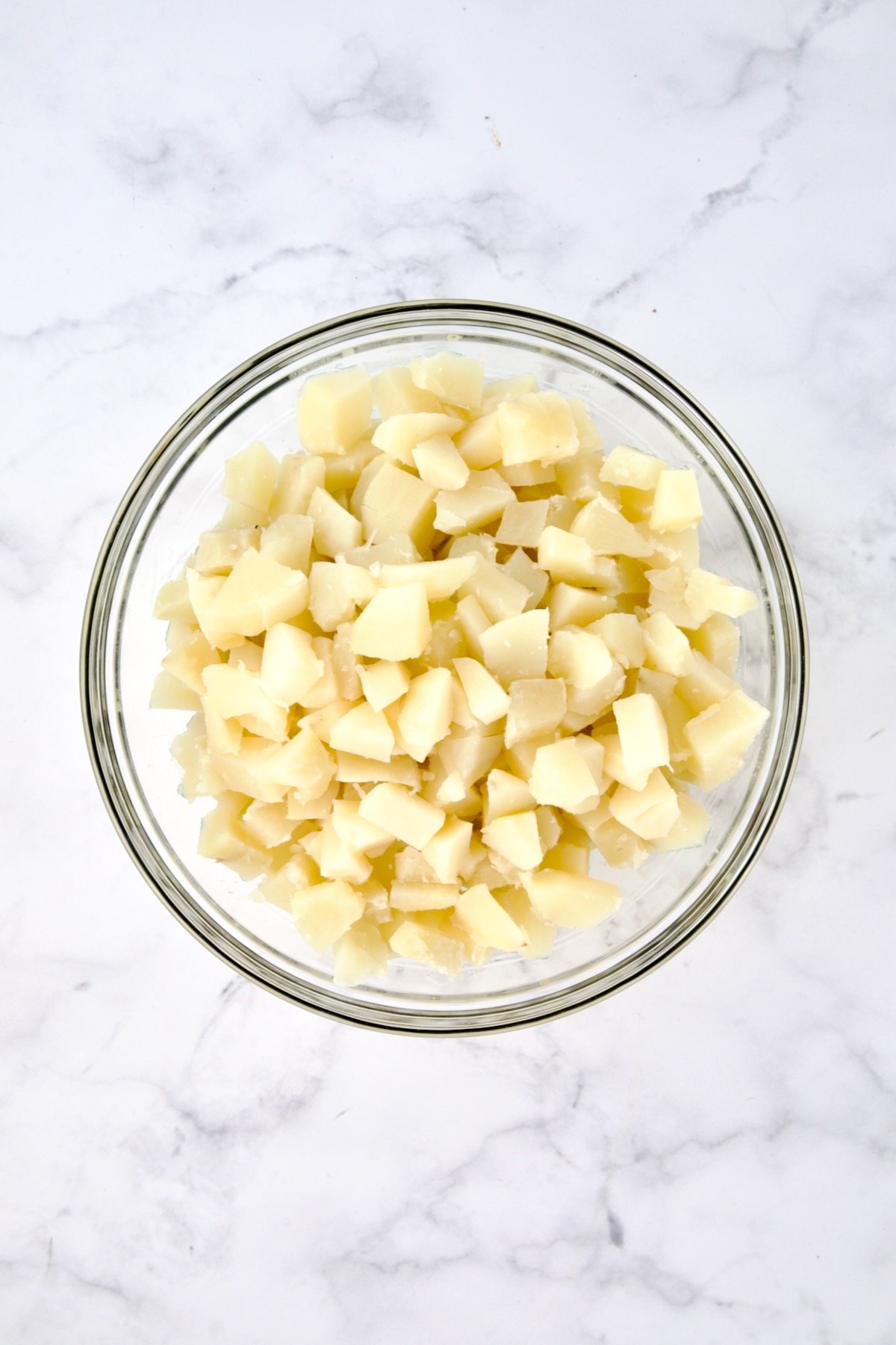 Cooked, cubed potatoes in glass bowl.
