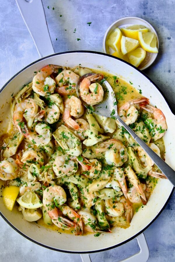 Shrimp Scampi with Artichokes in white enamel cast iron pan with serving spoon.