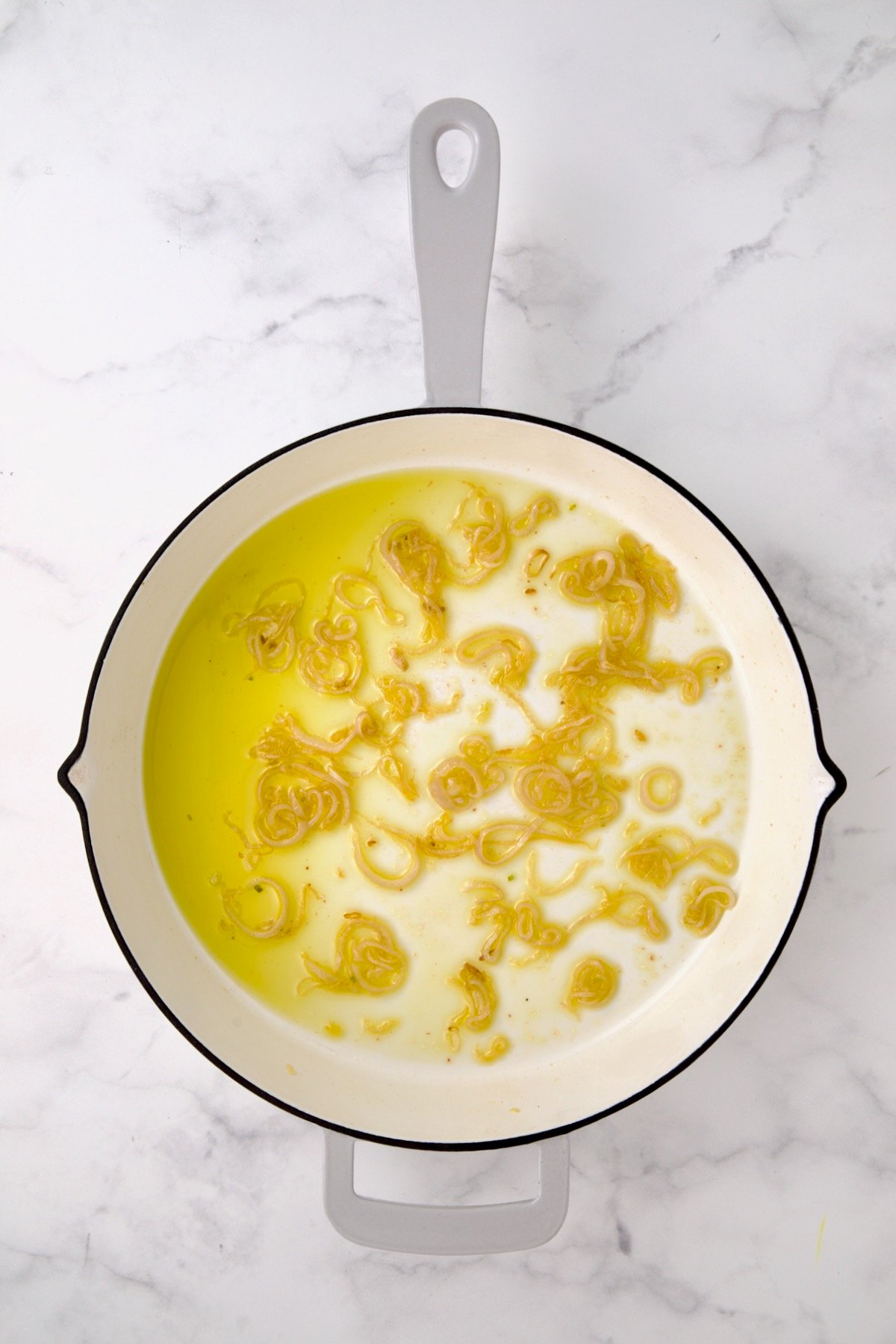 Softened shallots in olive oil white enamel cast iron pan.