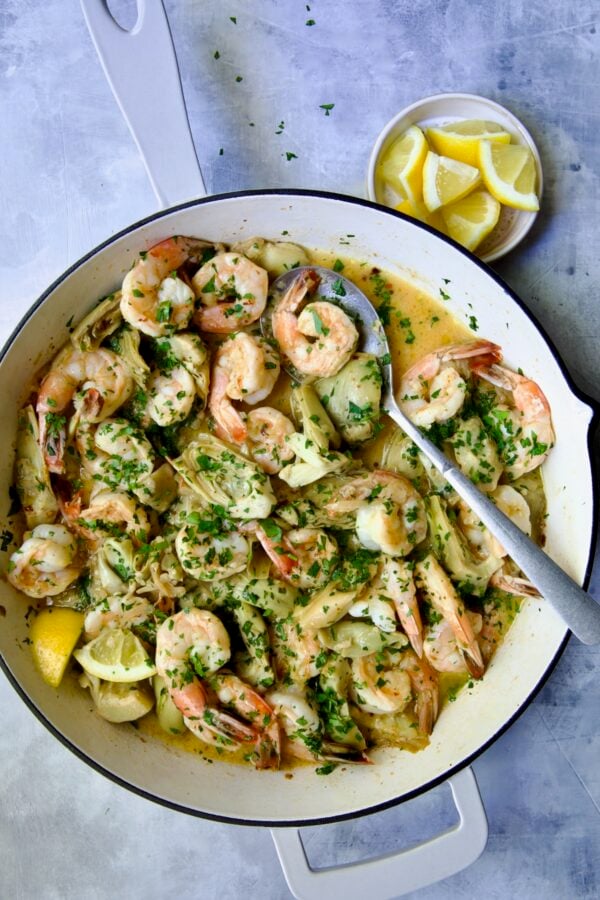 Shrimp Scampi with Artichokes in white enamel cast iron pan with serving spoon.