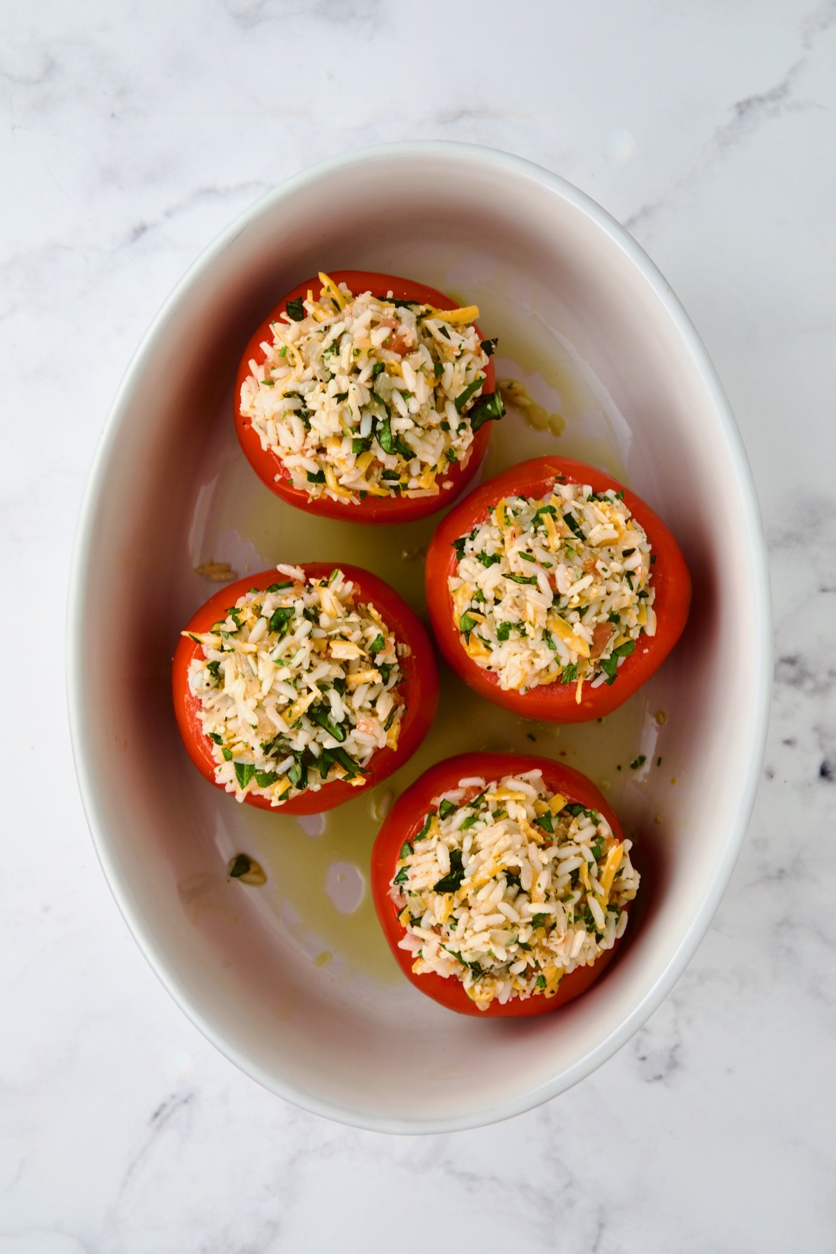 Four round cheese and rice-stuffed tomatoes in oval baking dish before being baked.