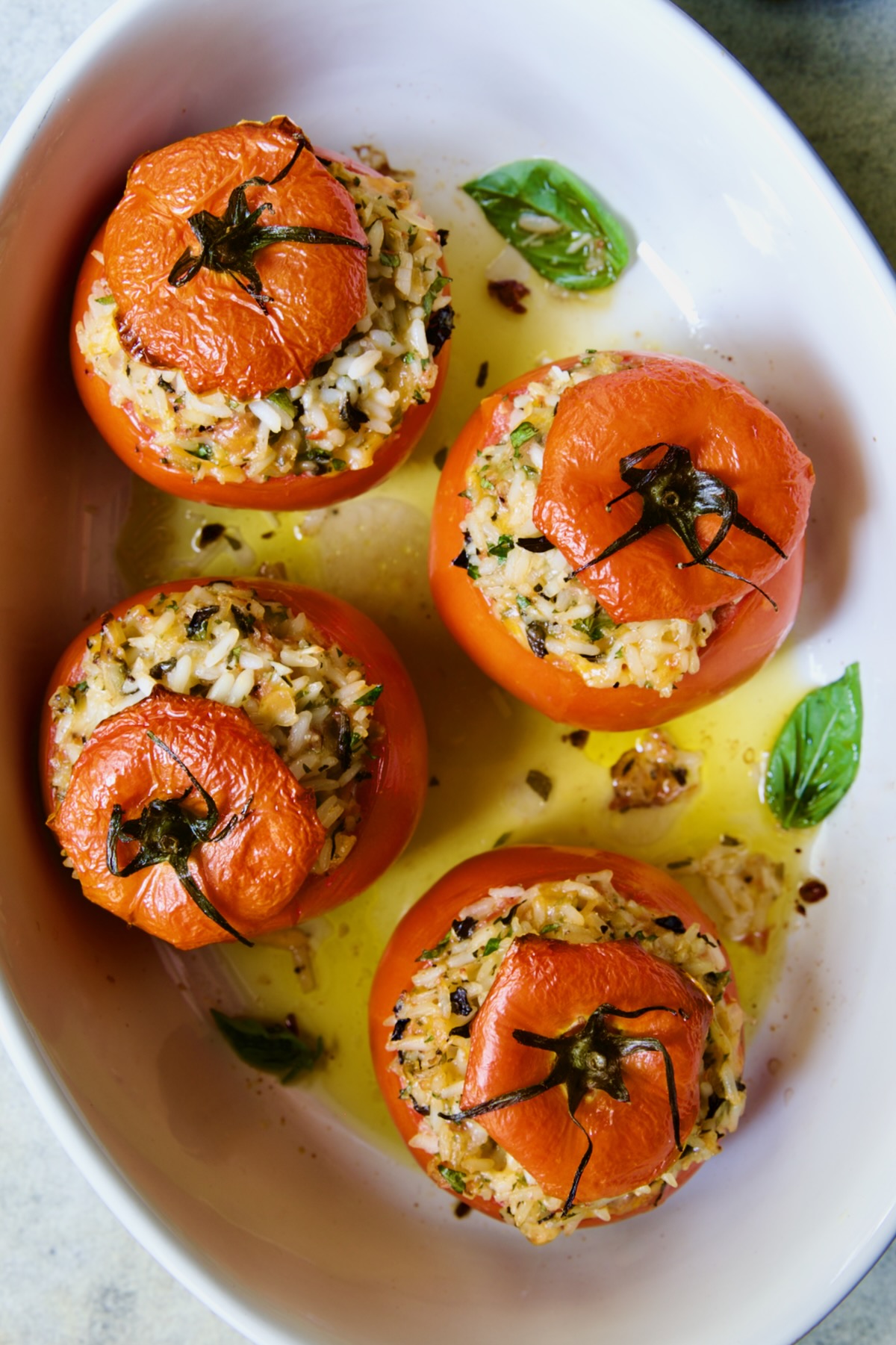 Four Cheesy Rice Stuffed Tomatoes in white oval baking dish with fresh basil leaves.