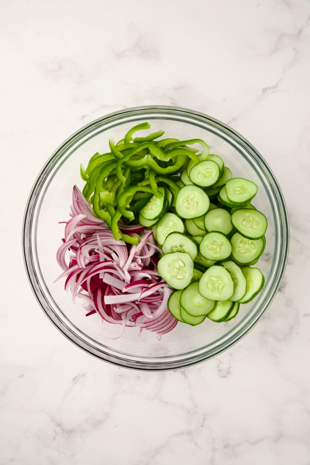 Sliced onion, green pepper and cucumbers in glass bowl.