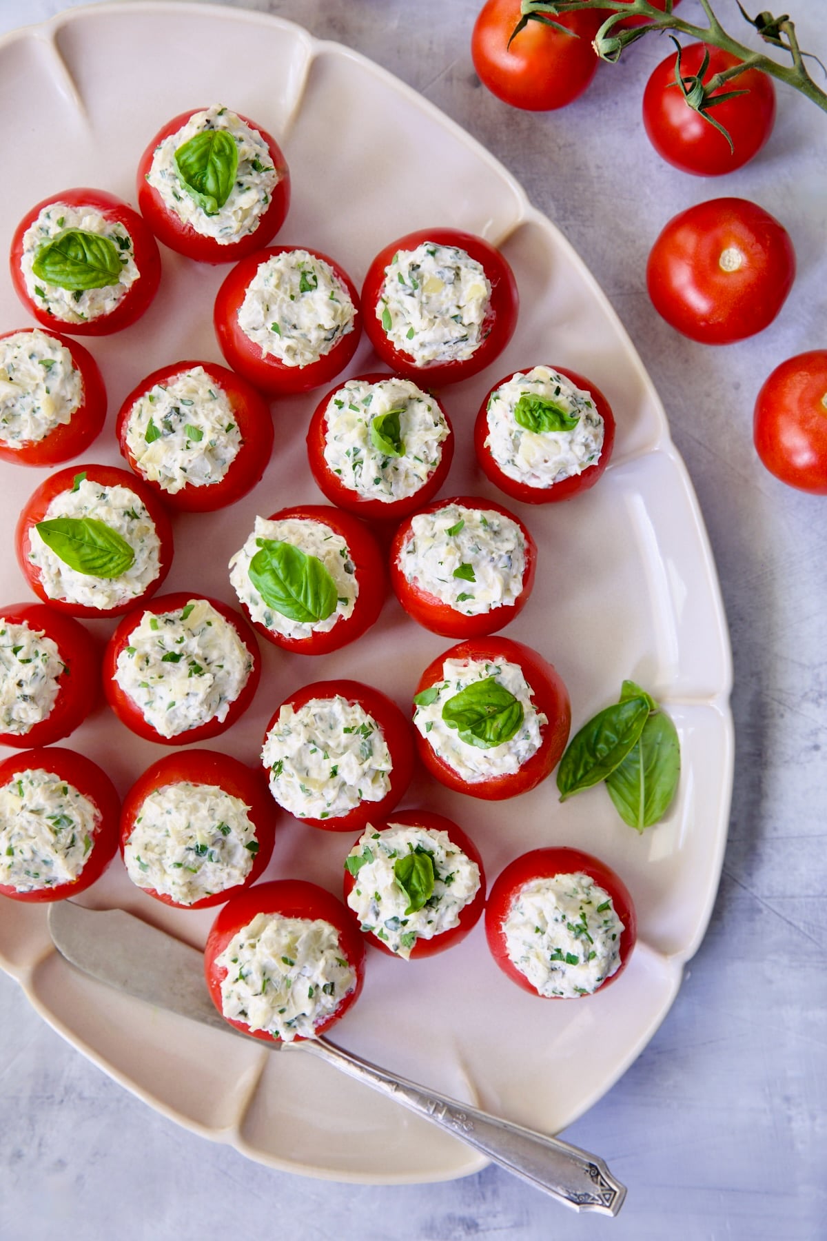 Cream Cheese and Artichoke Stuffed Tomatoes on oval white platter garnished with fresh basil leaves.