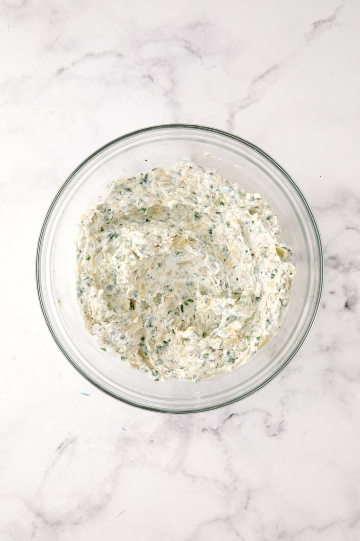 Ingredients for Cream Cheese and Artichoke Stuffed Tomatoes in glass bowl after being mixed together.