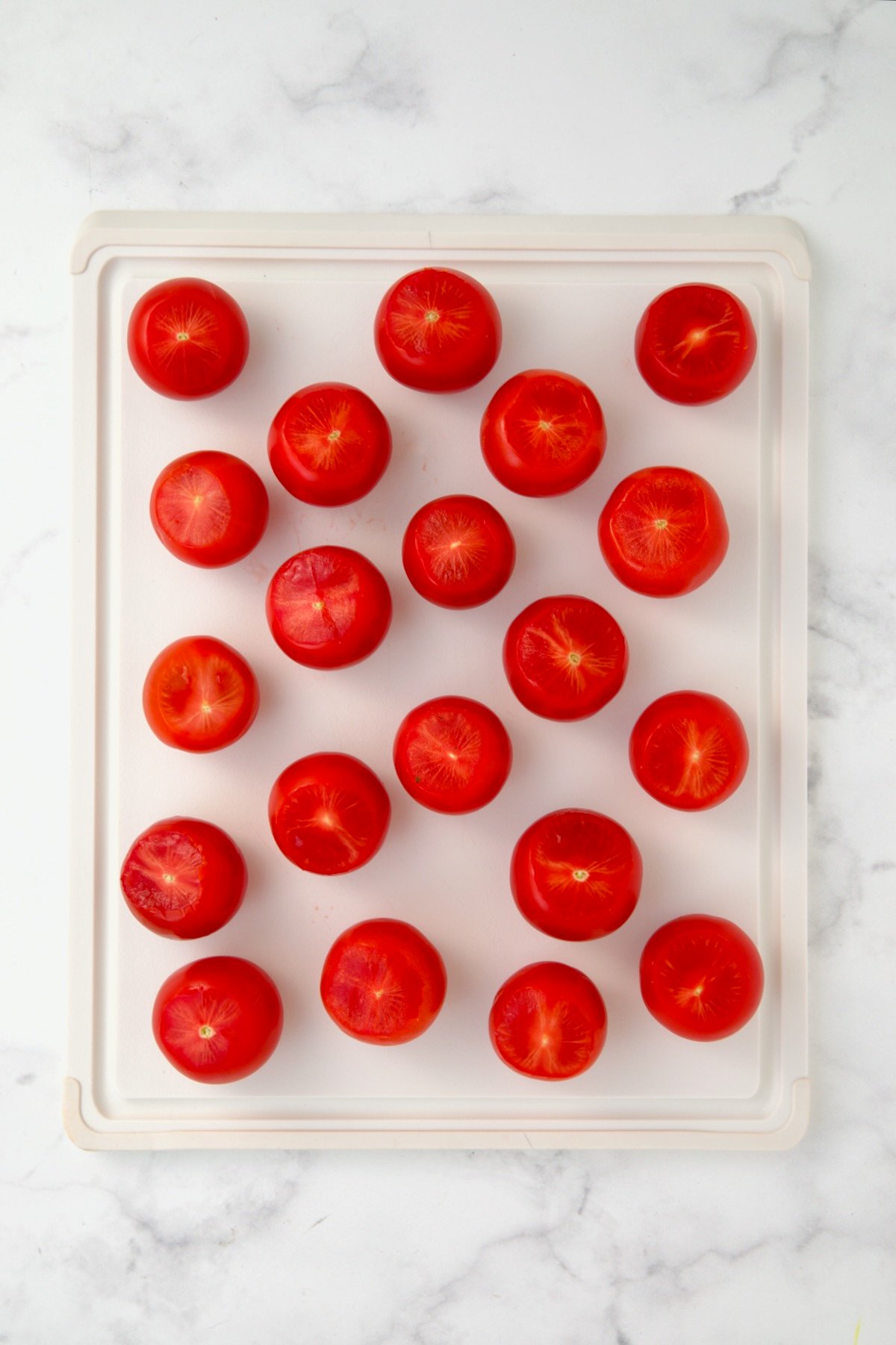 Campari tomatoes on white plastic cutting board with tops sliced off.