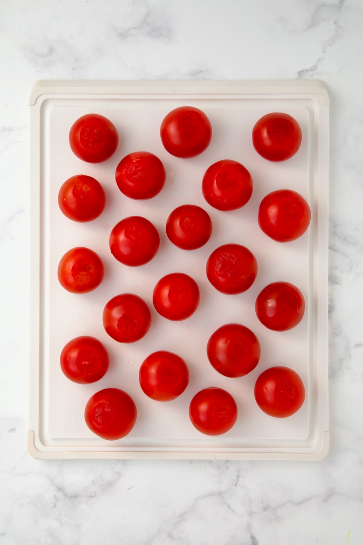 Campari tomatoes on white plastic cutting board with bottoms sliced off.