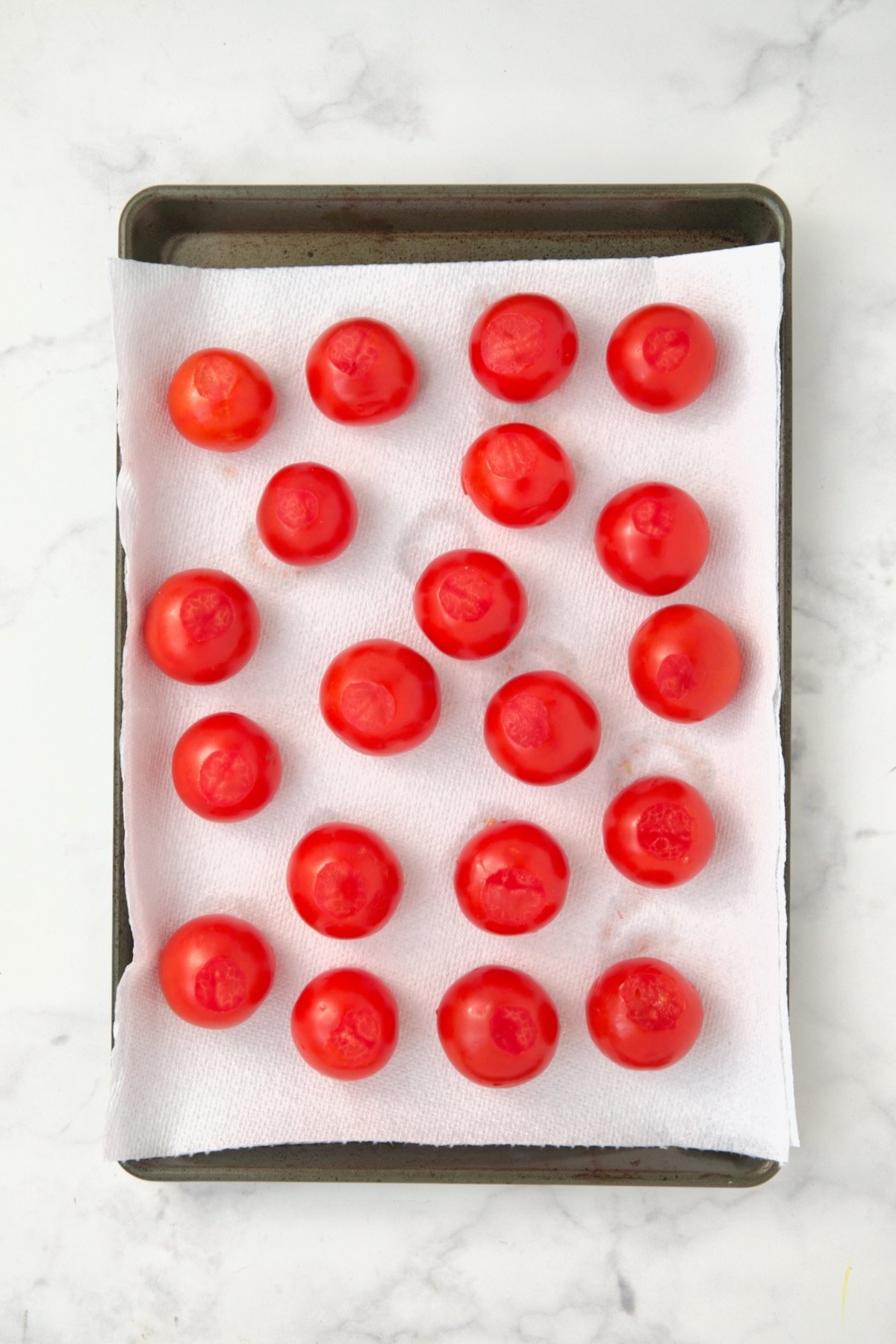 Hollowed out Campari tomatoes on paper towel-lined rimmed baking sheet draining.