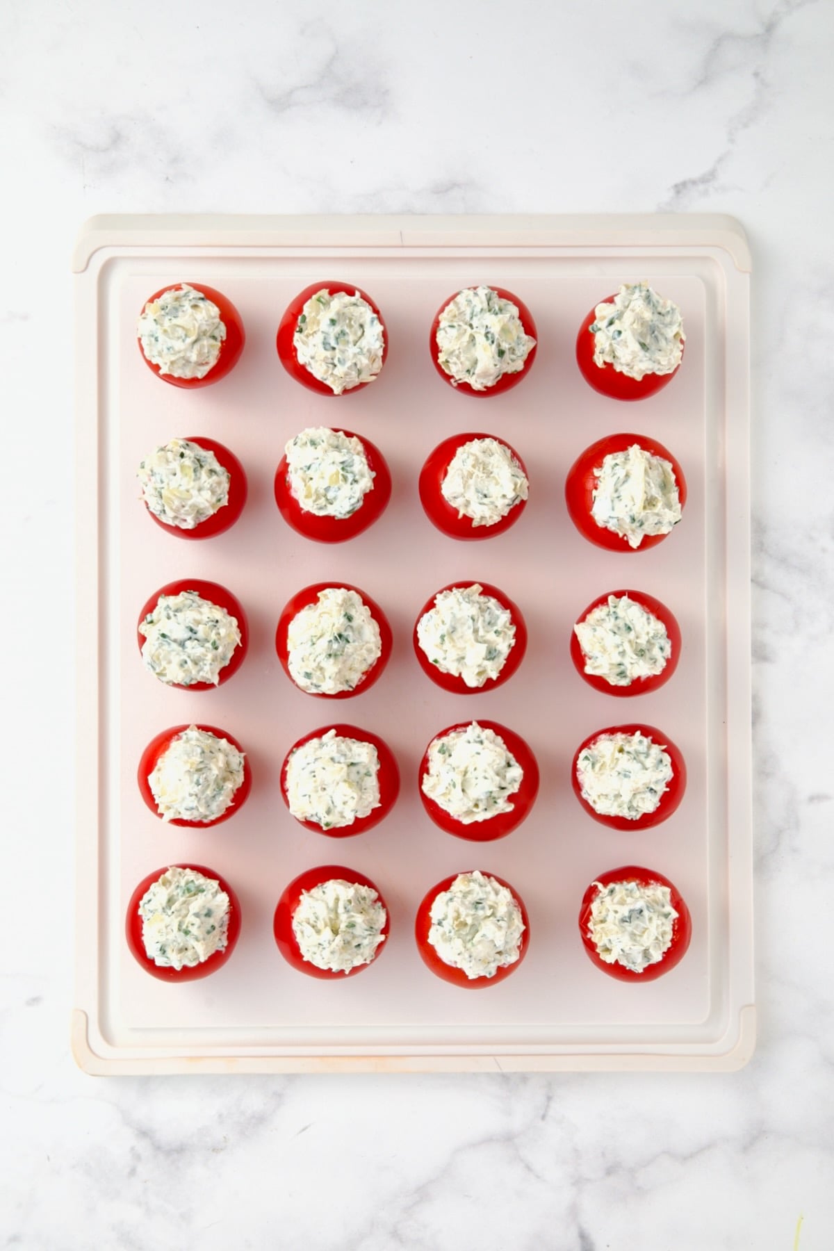 20 stuffed Campari tomatoes on white plastic cutting board.