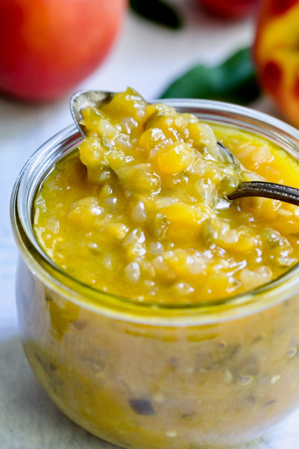 Peach Jalapeno Chutney in a glass jar with a spoon holding some.