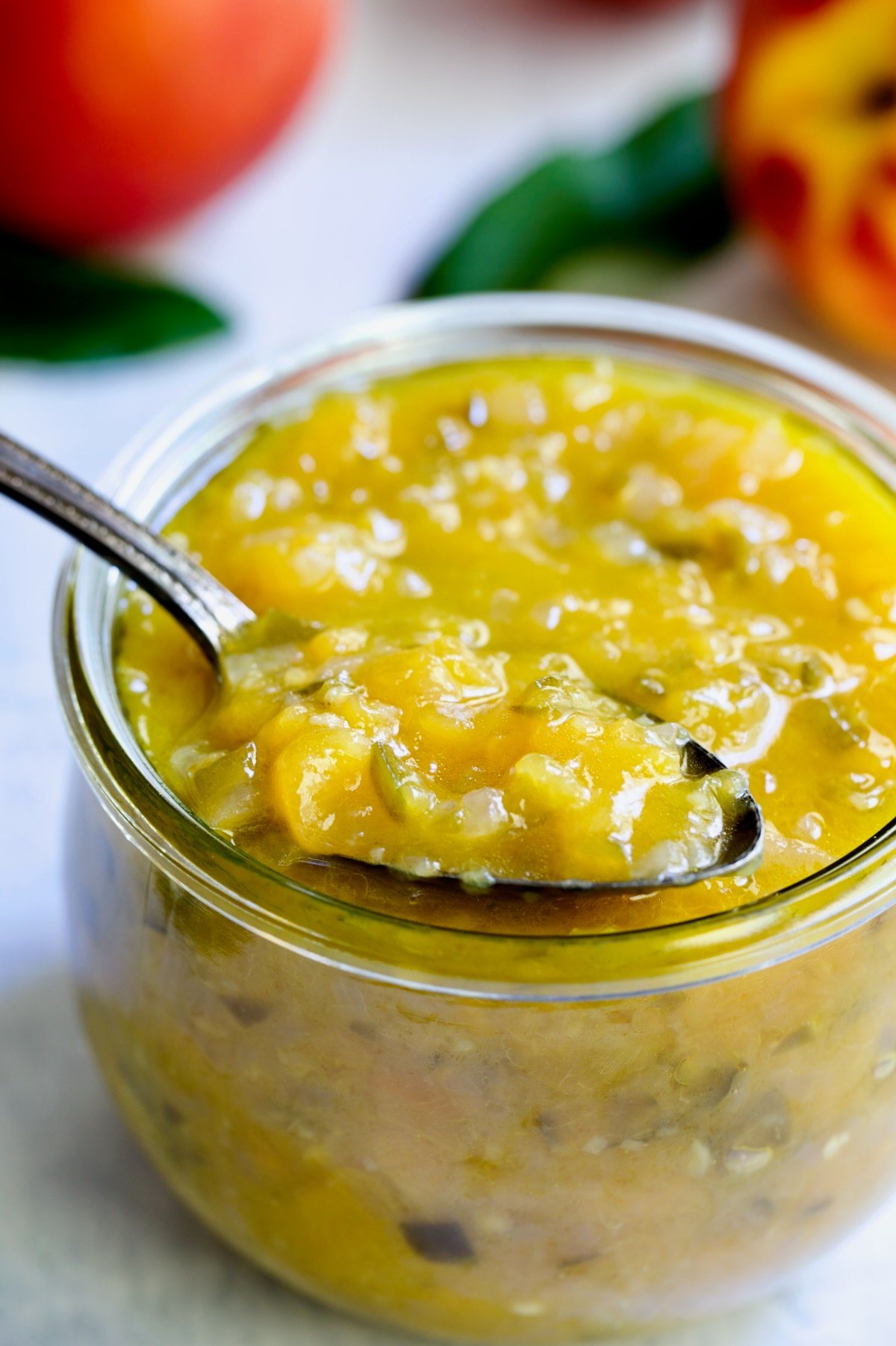 Peach Jalapeno Chutney in a glass jar with a spoon holding some to show detail.