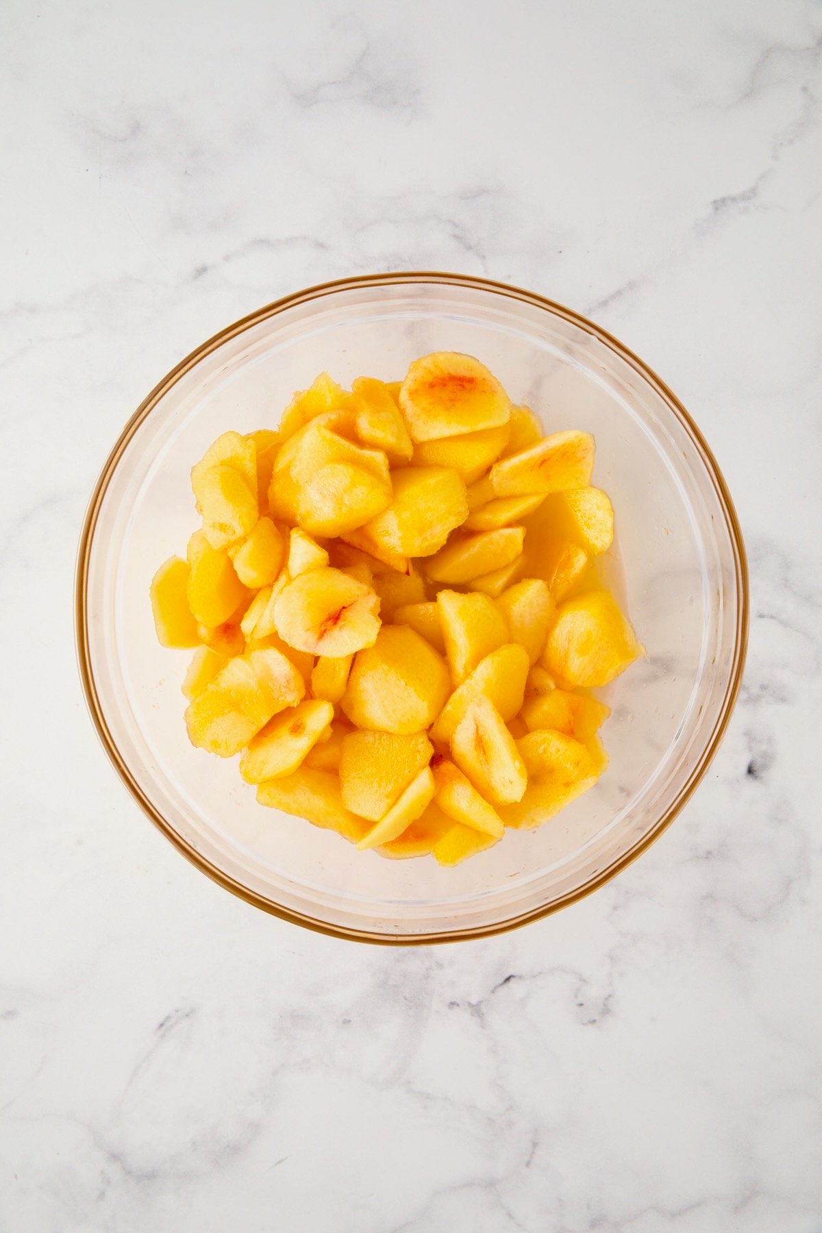 Peeled peach chunks in glass bowl.