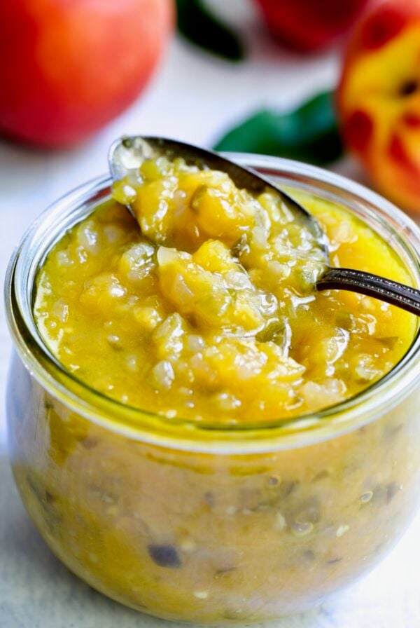 Peach Jalapeno Chutney in a glass jar with a spoon holding some.