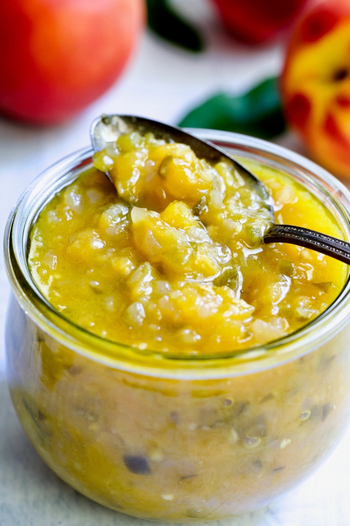 Peach Jalapeno Chutney in a glass jar with a spoon holding some.