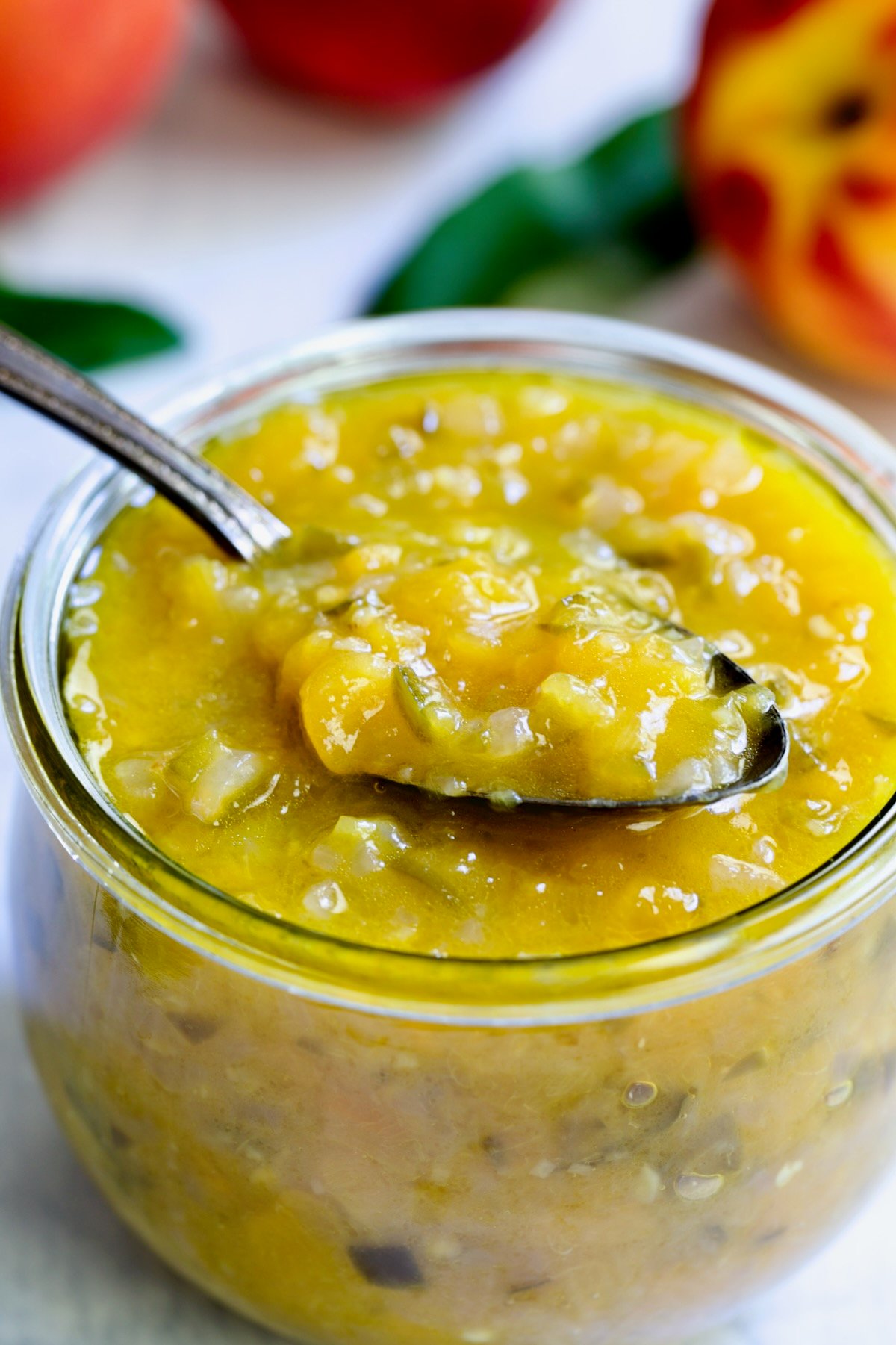 Peach Jalapeno Chutney in a glass jar with a spoon holding some.