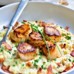 One serving of Seared Sea Scallops with Smoky Sweet Corn Puree on white plate with fork garnished with fresh chives.