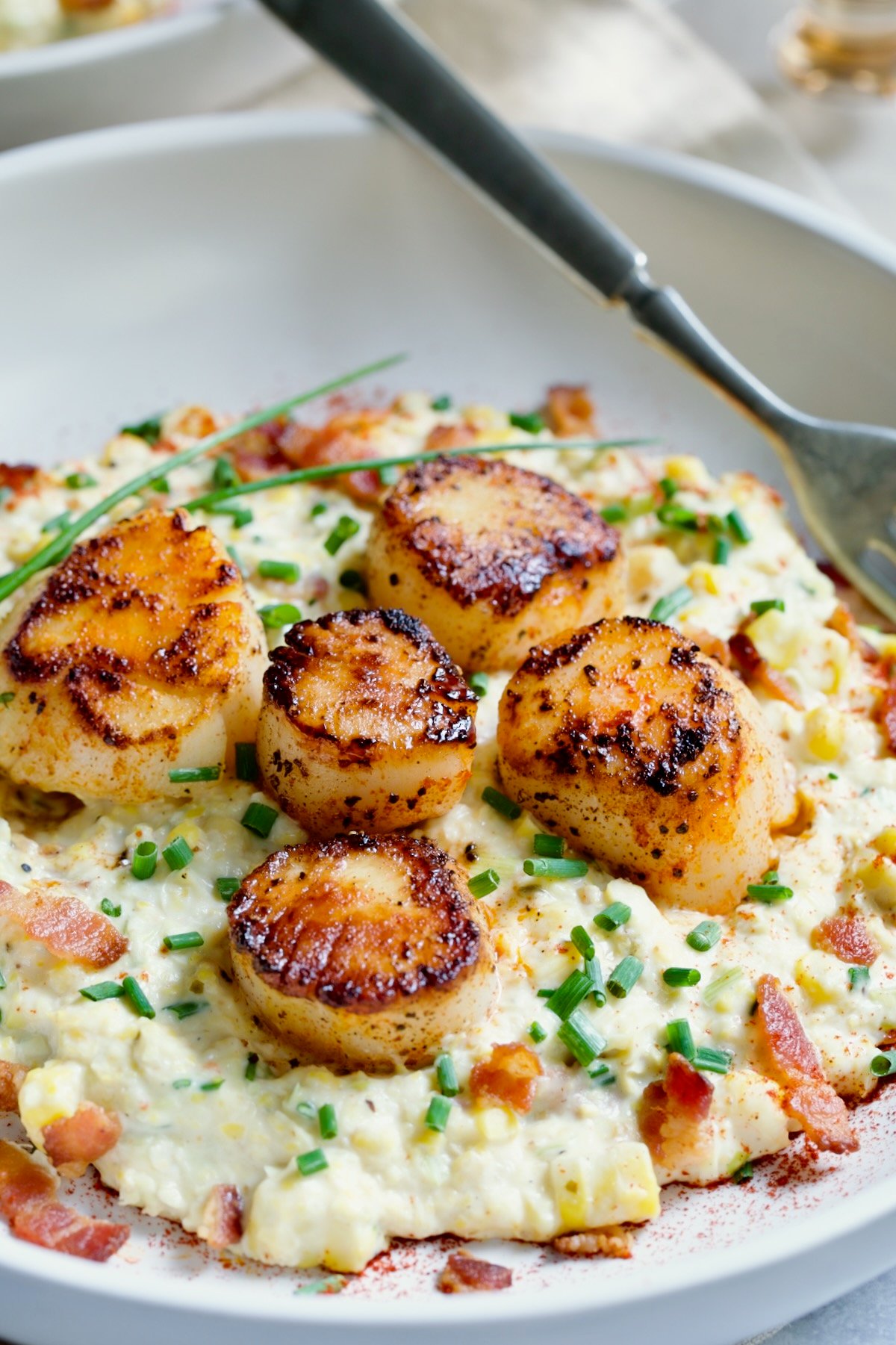 One serving of Seared Sea Scallops with Smoky Sweet Corn Puree on white plate with fork.