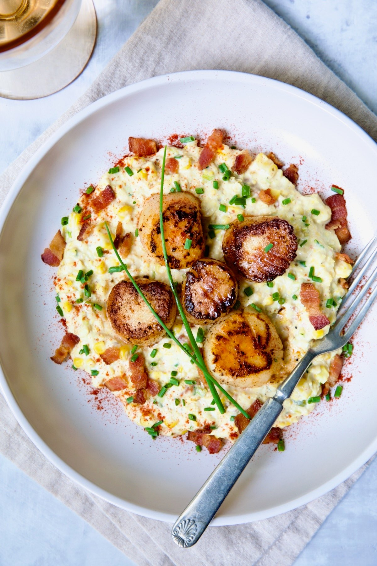 One serving of Seared Sea Scallops with Smoky Sweet Corn Puree on white plate with fork garnished with fresh chives.