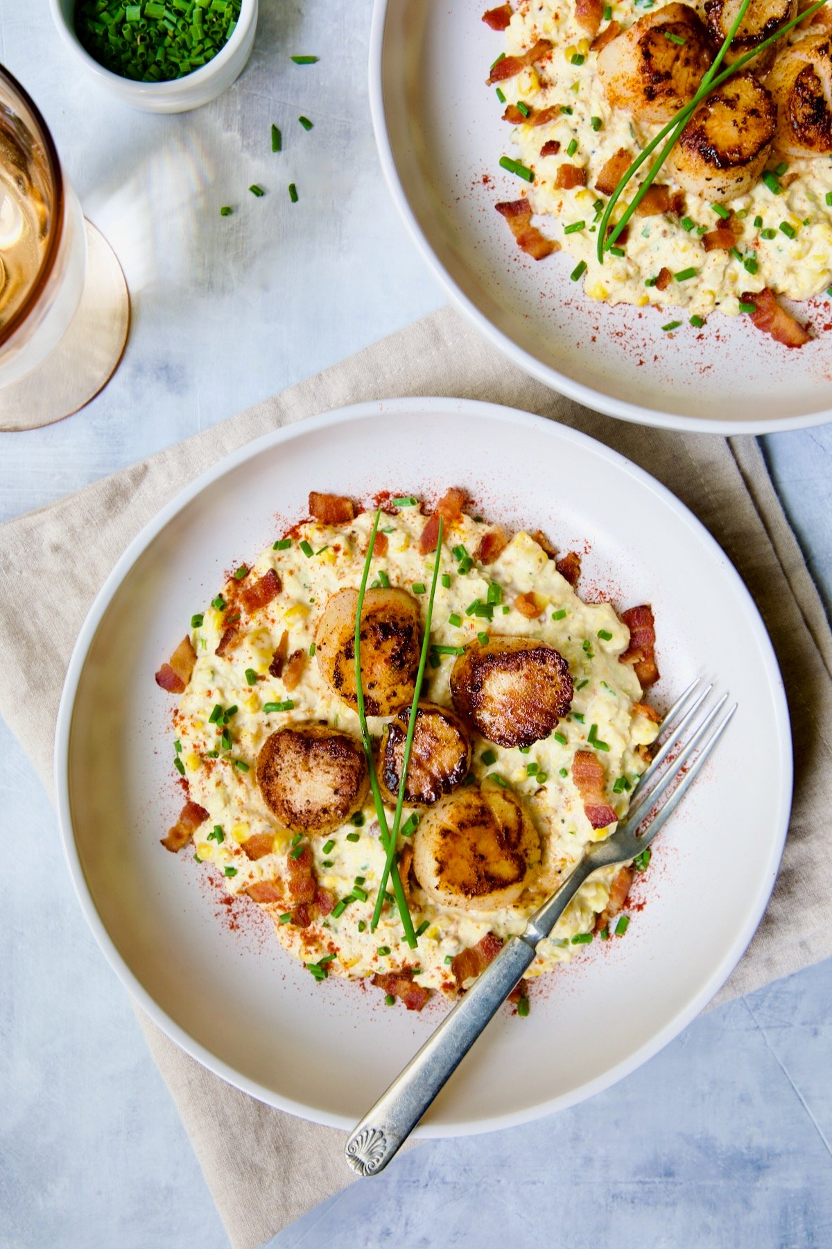 Two servings of Seared Sea Scallops with Smoky Sweet Corn Puree on a white plate with fork.