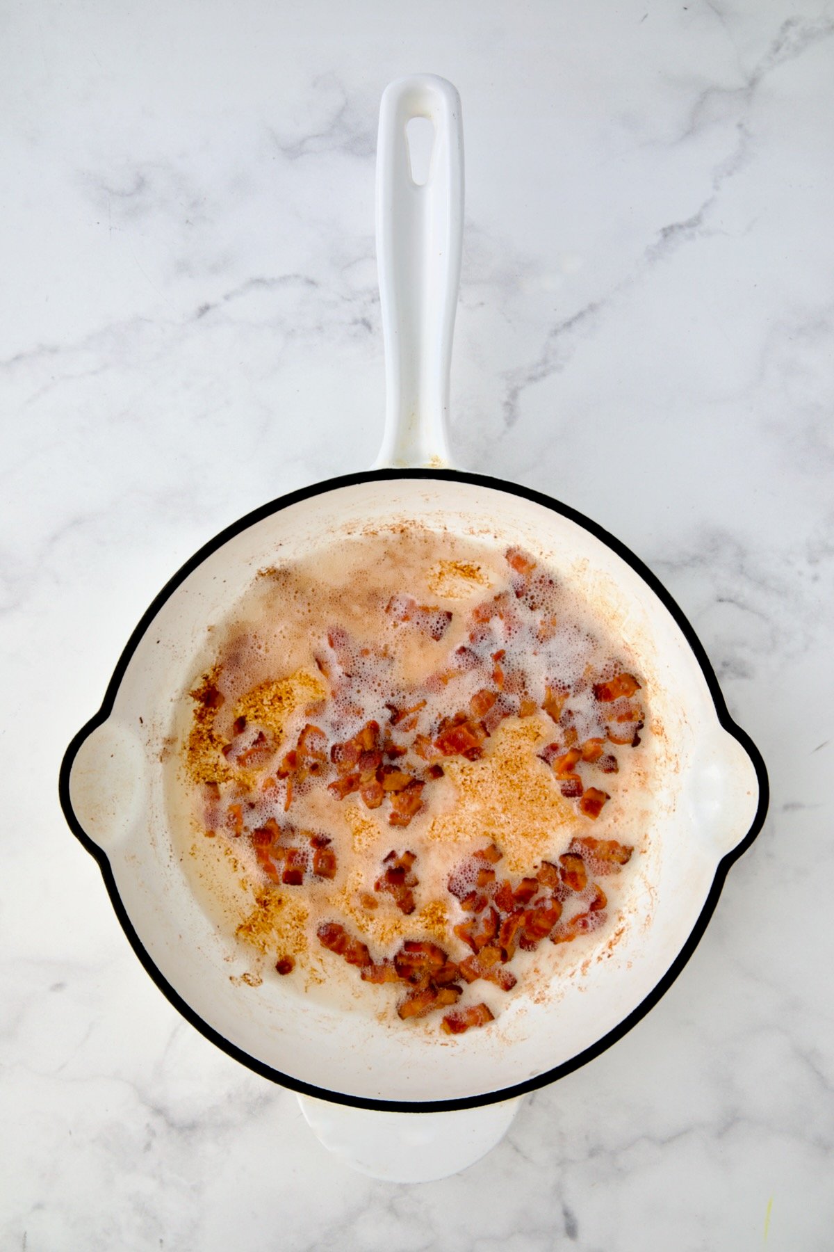 Cooked crispy bacon in white enamel cast iron skillet.