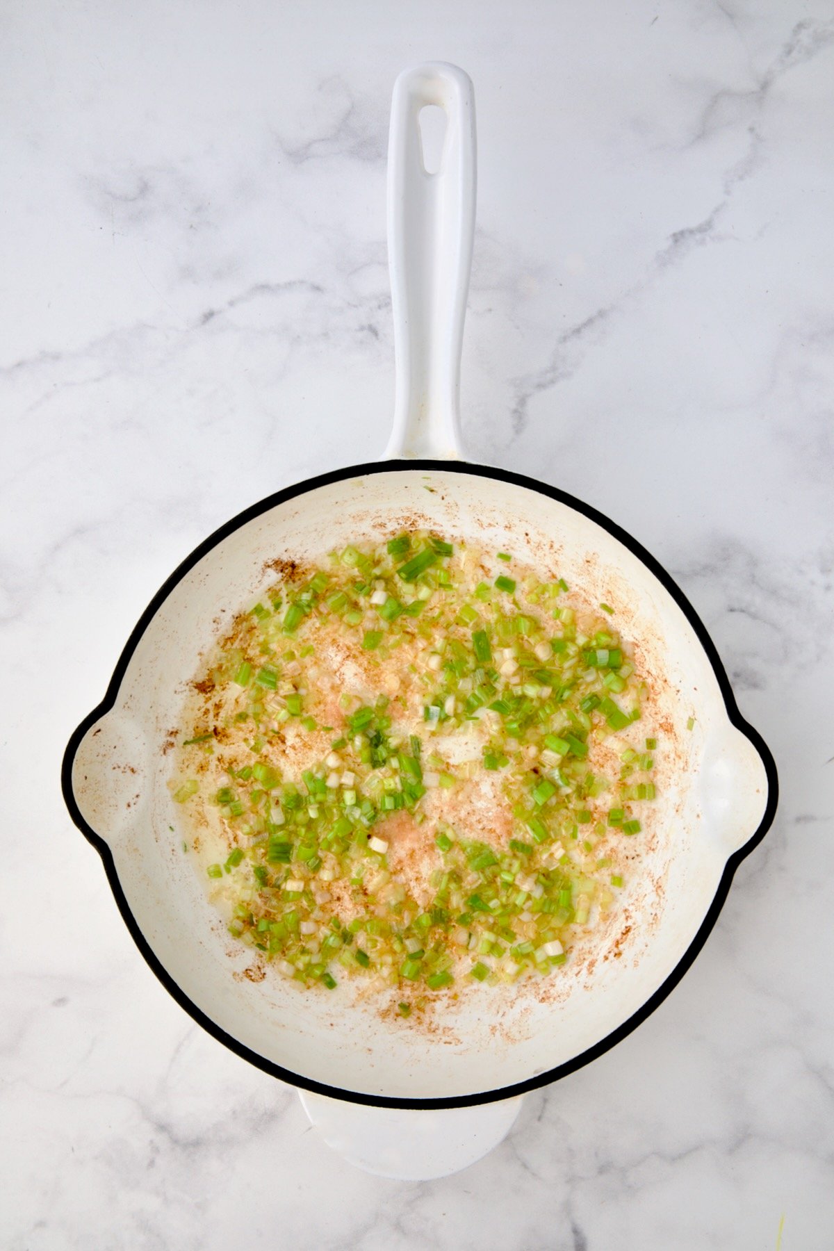 Cooked scallions in white enamel cast iron skillet.