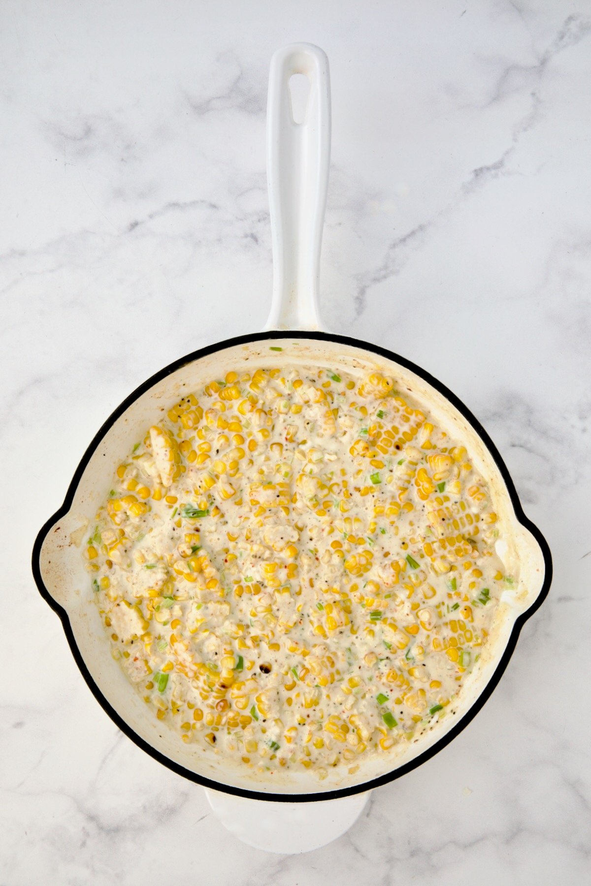 Cream cheese and heavy cream added to corn in white enamel cast iron skillet after being stirred in.