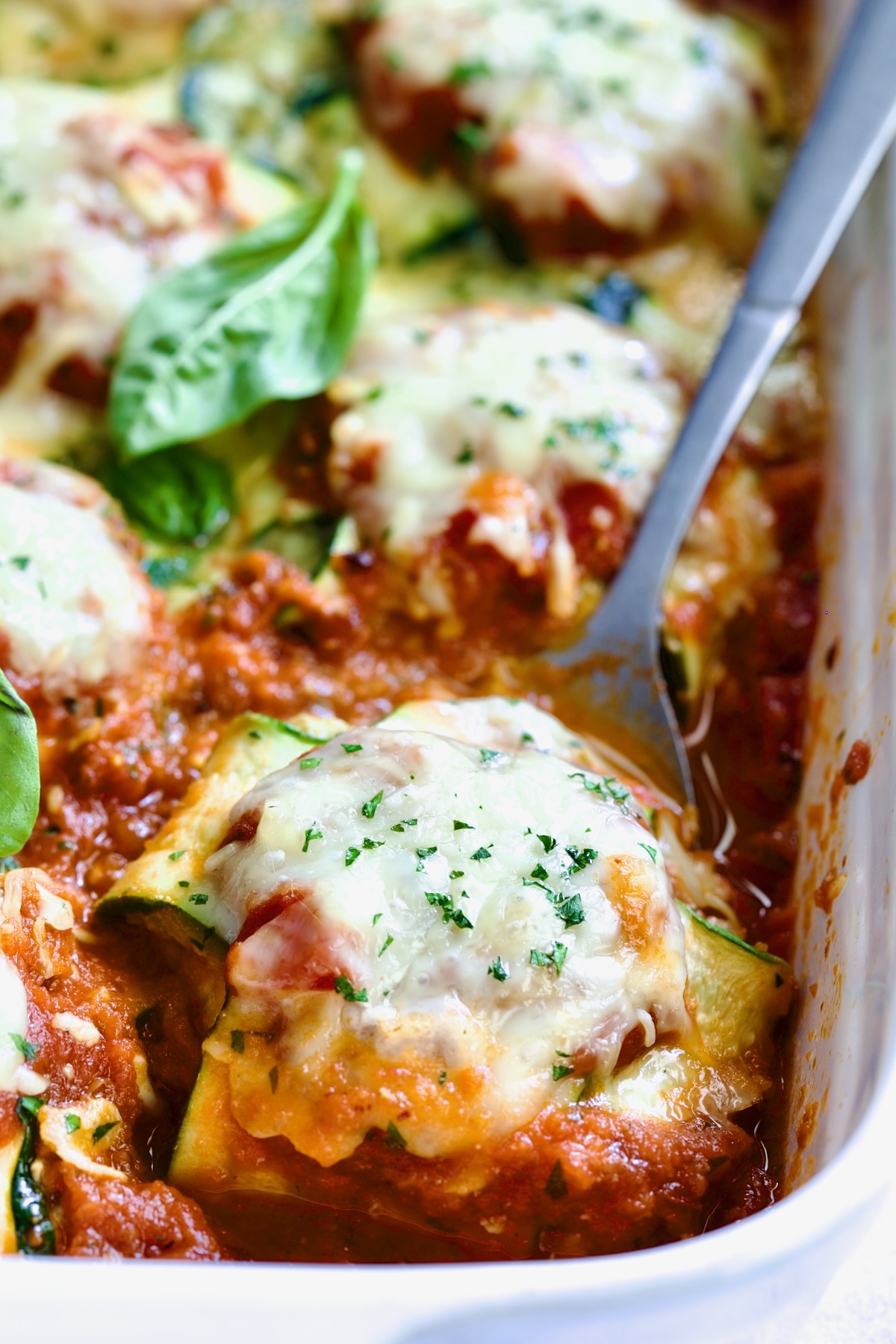 Zucchini Ravioli in white baking dish with serving spoon.