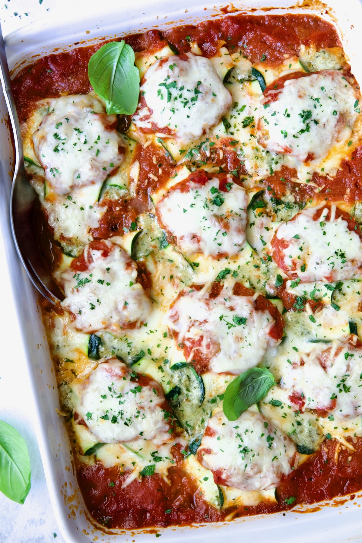 Zucchini Ravioli in white baking dish with serving spoon.