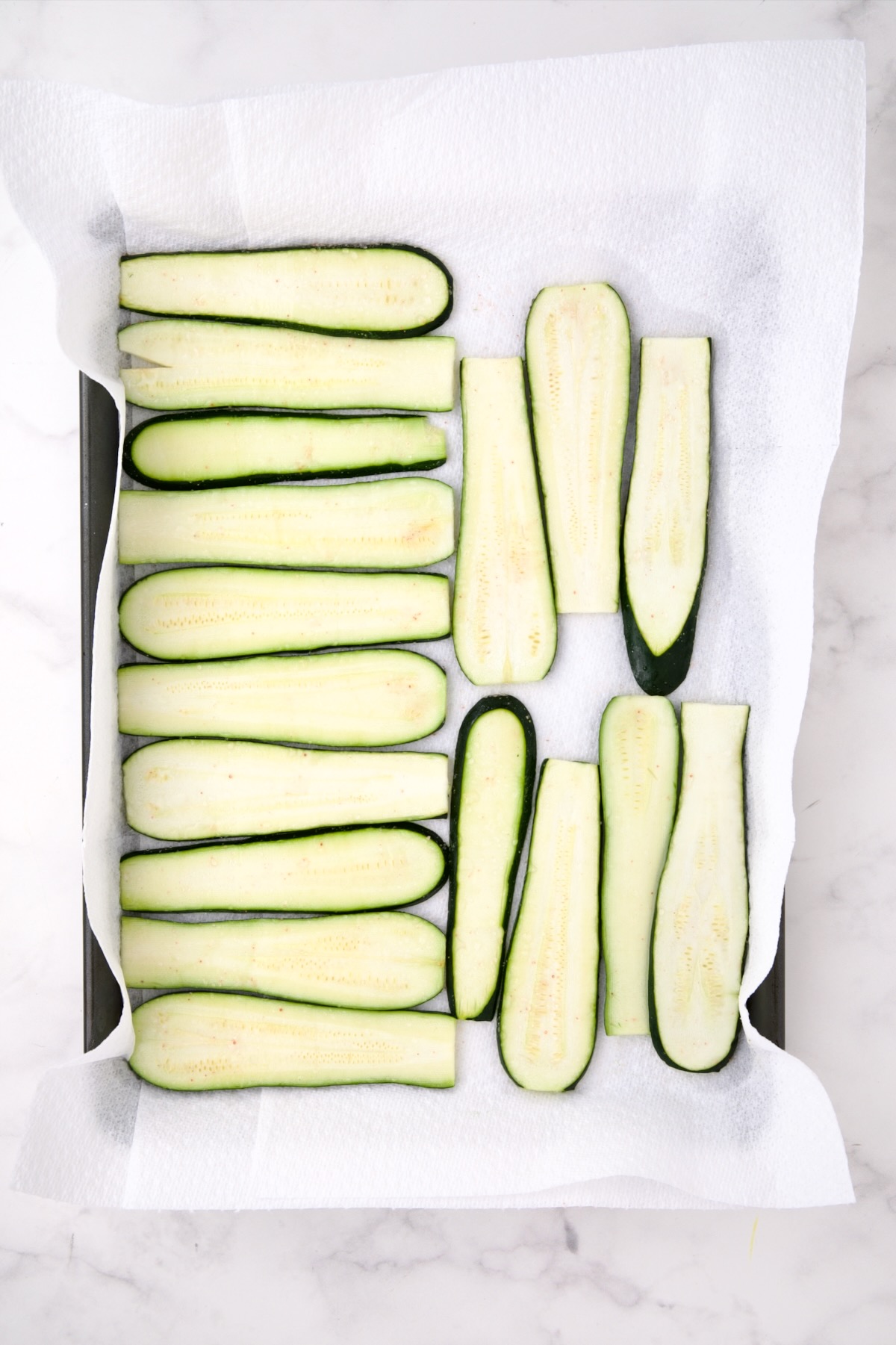 Thinly sliced salted zucchini slices on paper towel lined baking sheet.