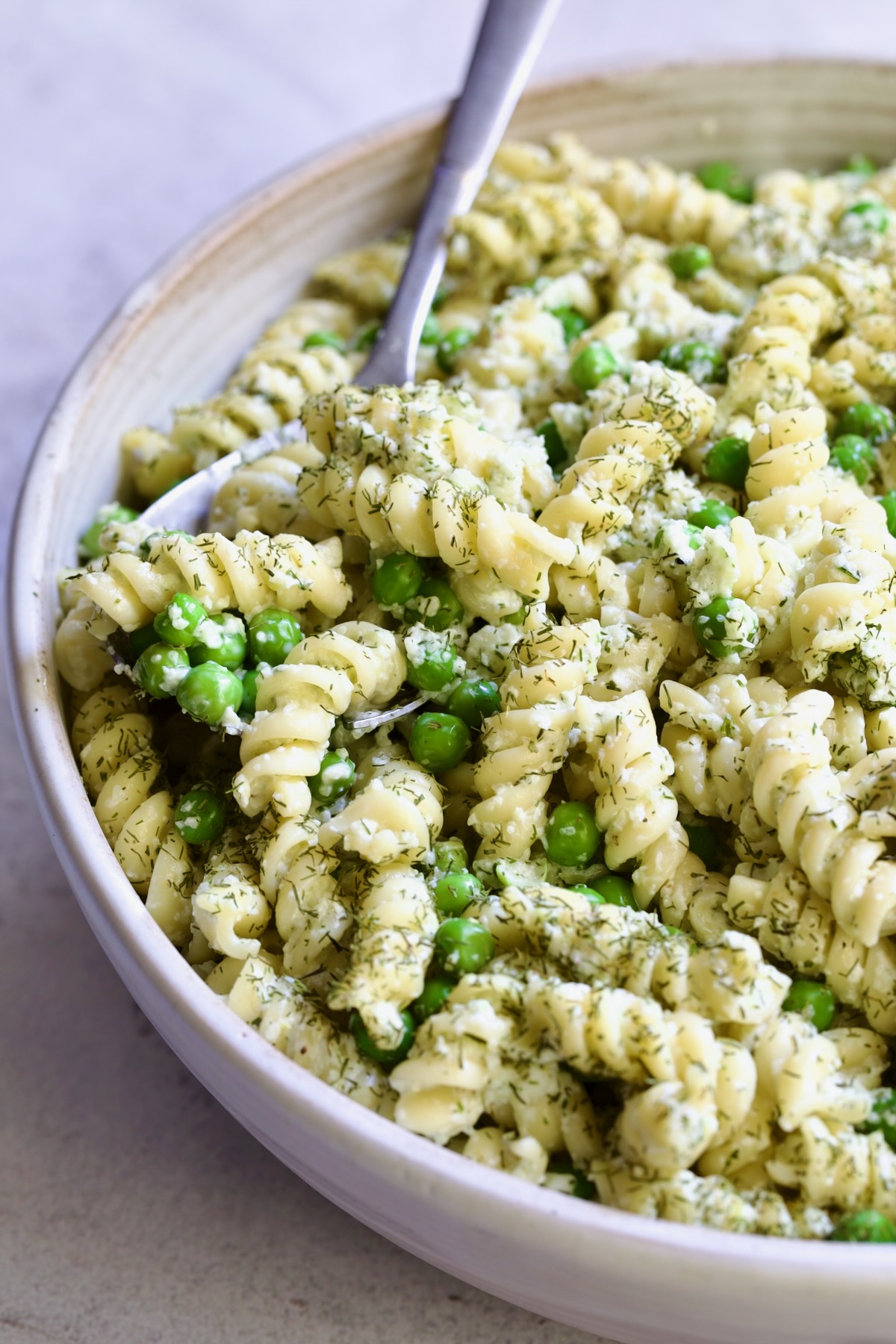 Creamy Cucumber Pasta Salad in white serving bowl with serving spoon.