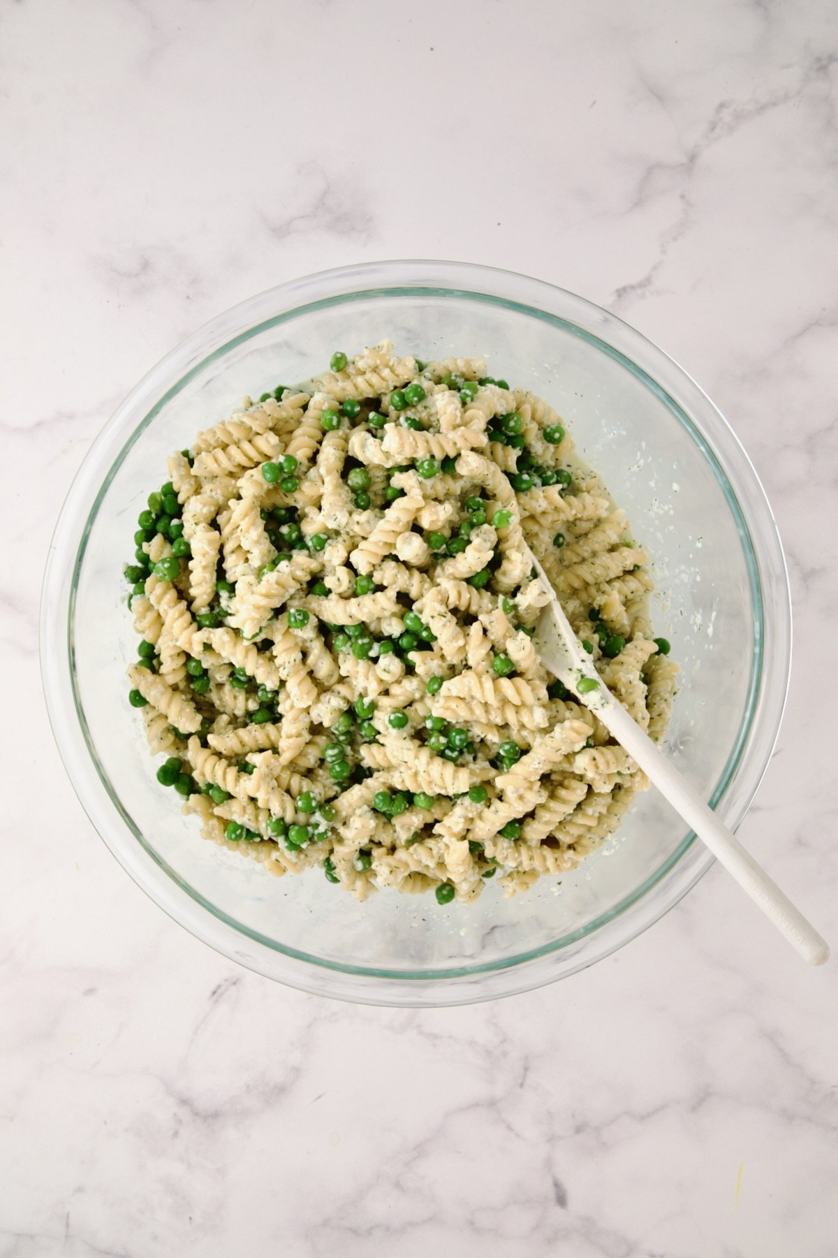 Cucumber Pasta Salad mixed together in glass bowl with white mixing spoon.