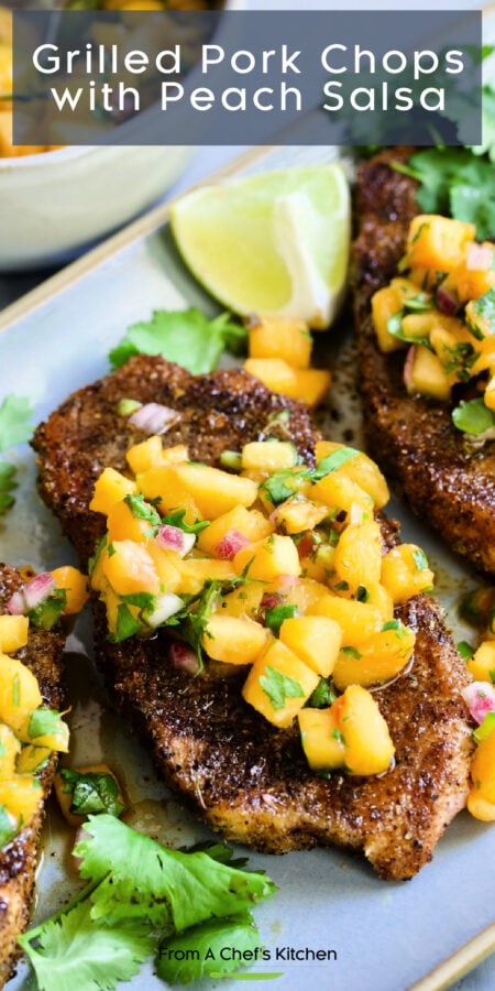Pinterest graphic for Grilled Pork Chops with Peach Salsa showing them on a gray oval platter garnished with lime wedges and fresh cilantro.
