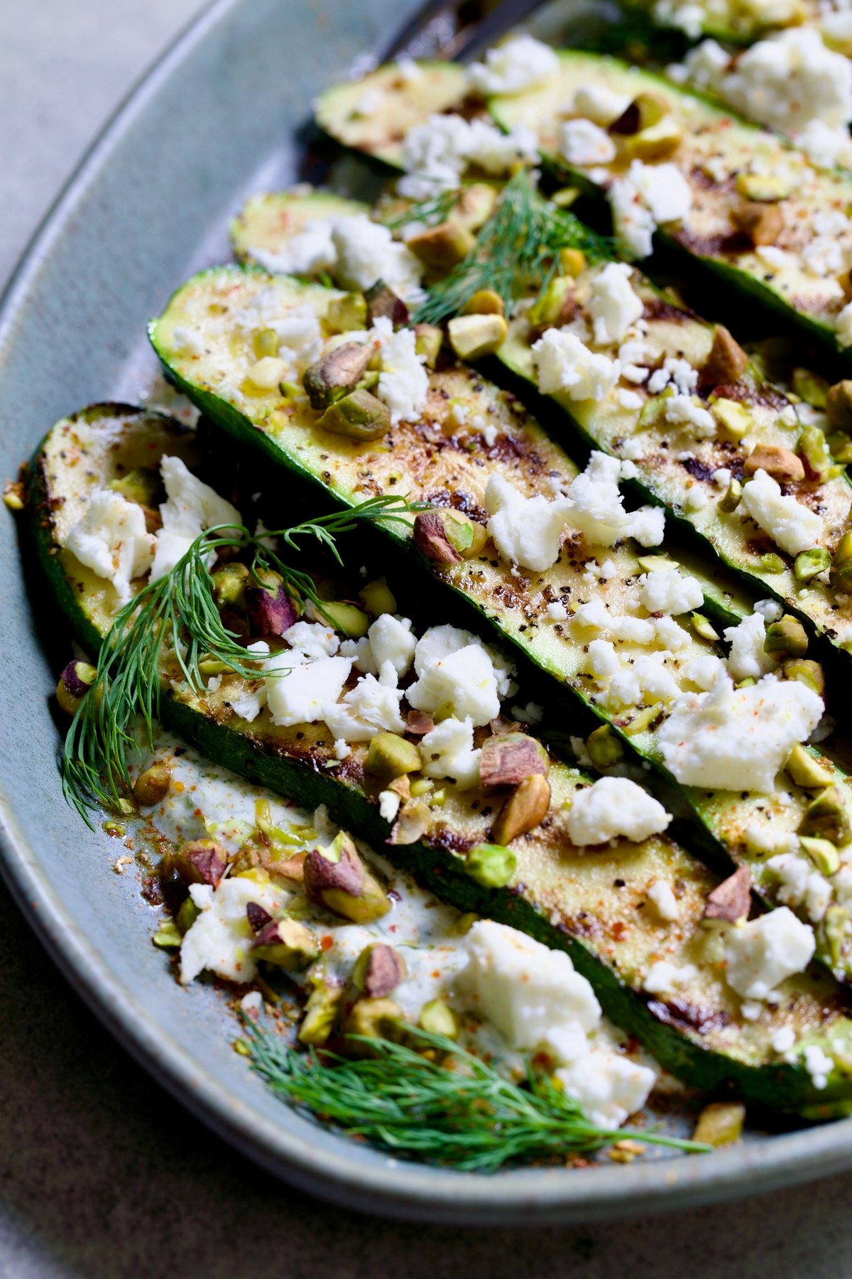 Mediterranean Grilled Zucchini with Dill Yogurt and Feta on blue platter garnished with pistachios and fresh dill sprigs.