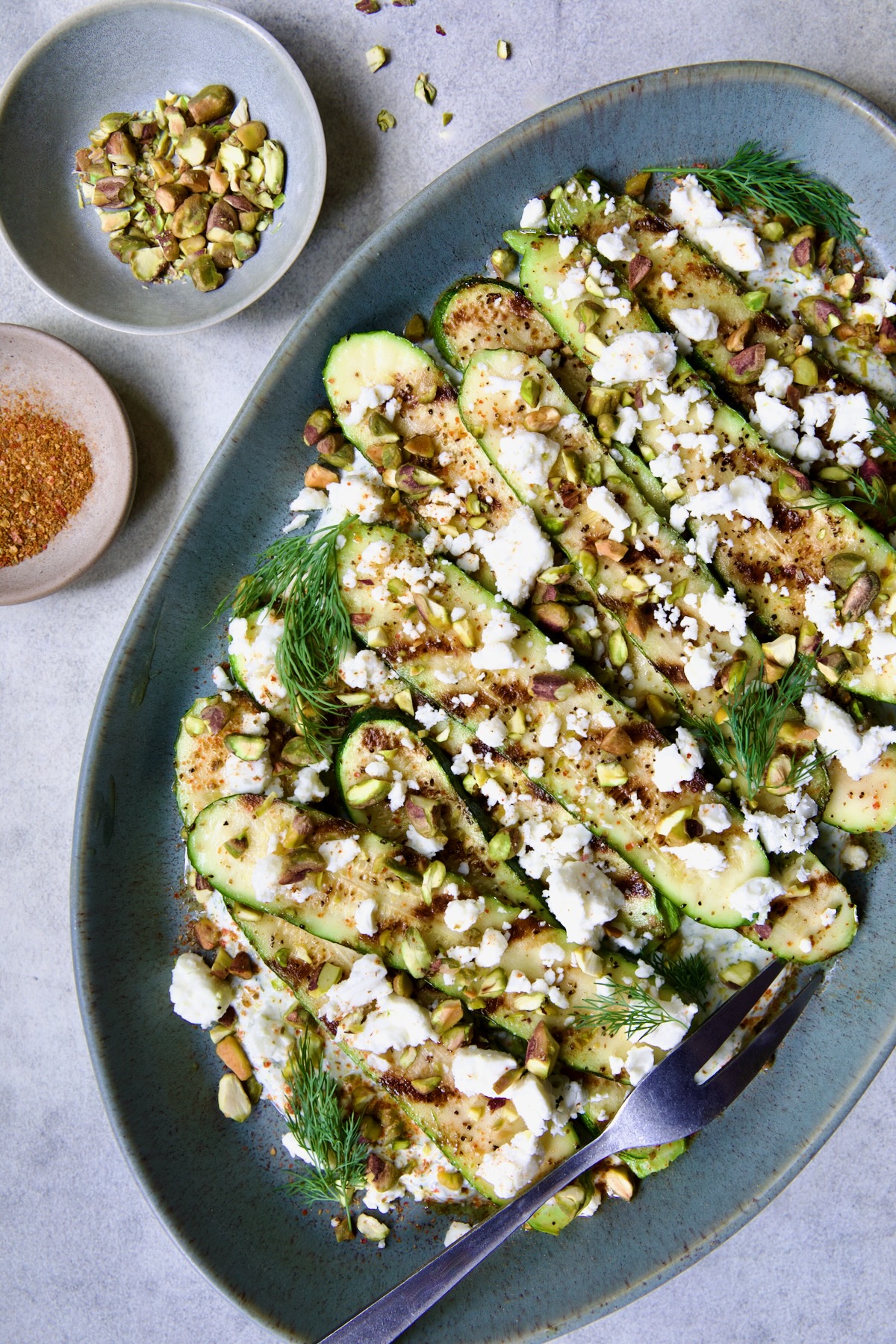 Mediterranean Grilled Zucchini with Dill Yogurt and Feta on blue platter garnished with pistachios and fresh dill sprigs.