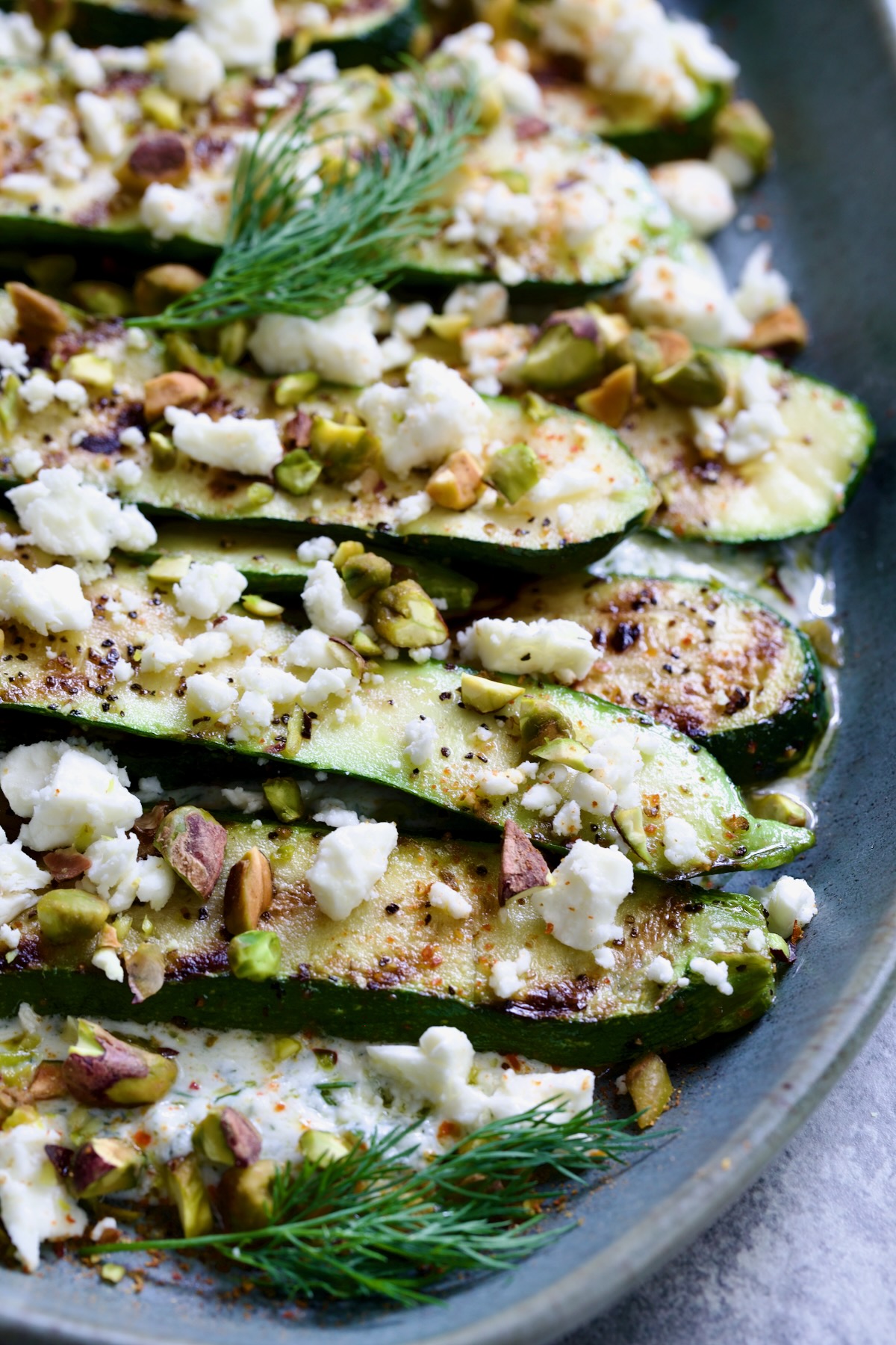Mediterranean Grilled Zucchini with Dill Yogurt and Feta on blue platter garnished with pistachios and fresh dill sprigs.