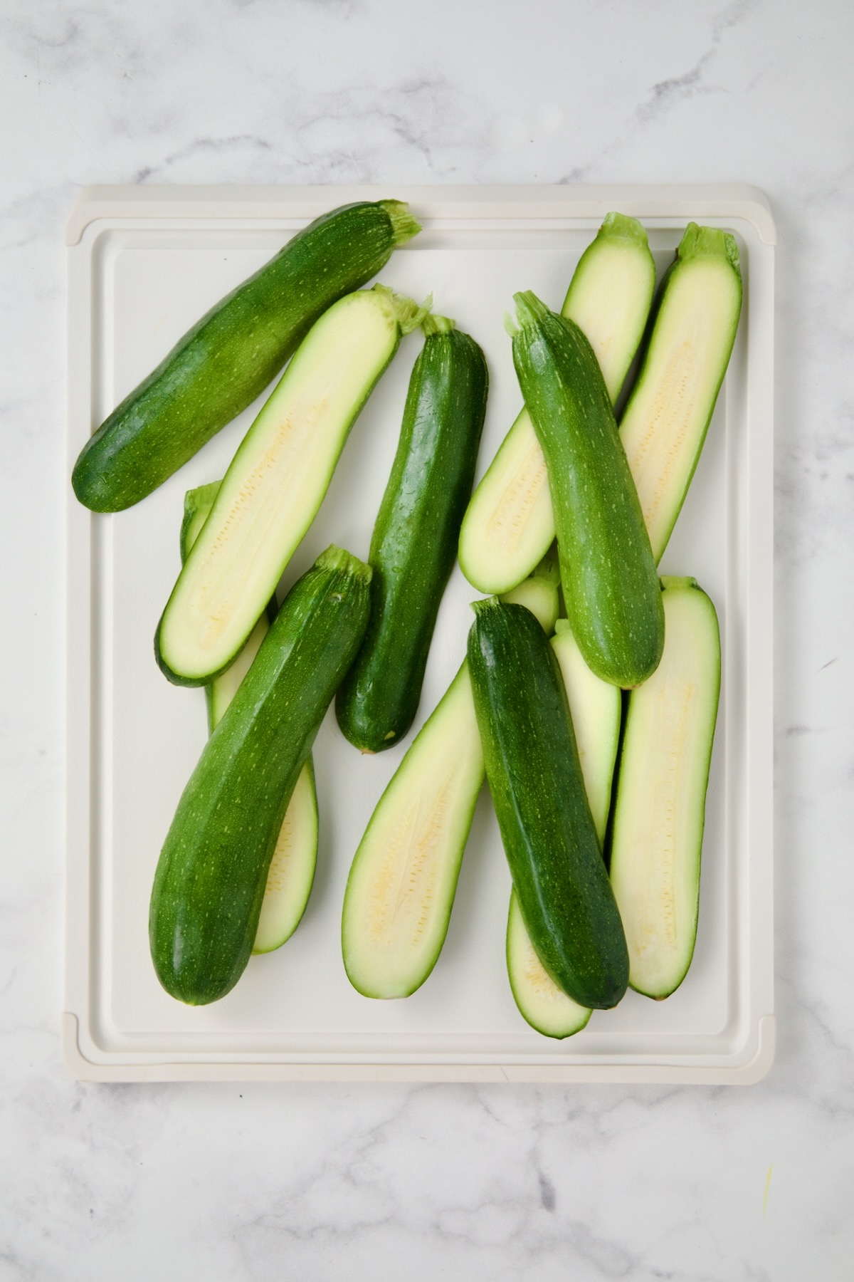 Sliced zucchini on white plastic cutting board.