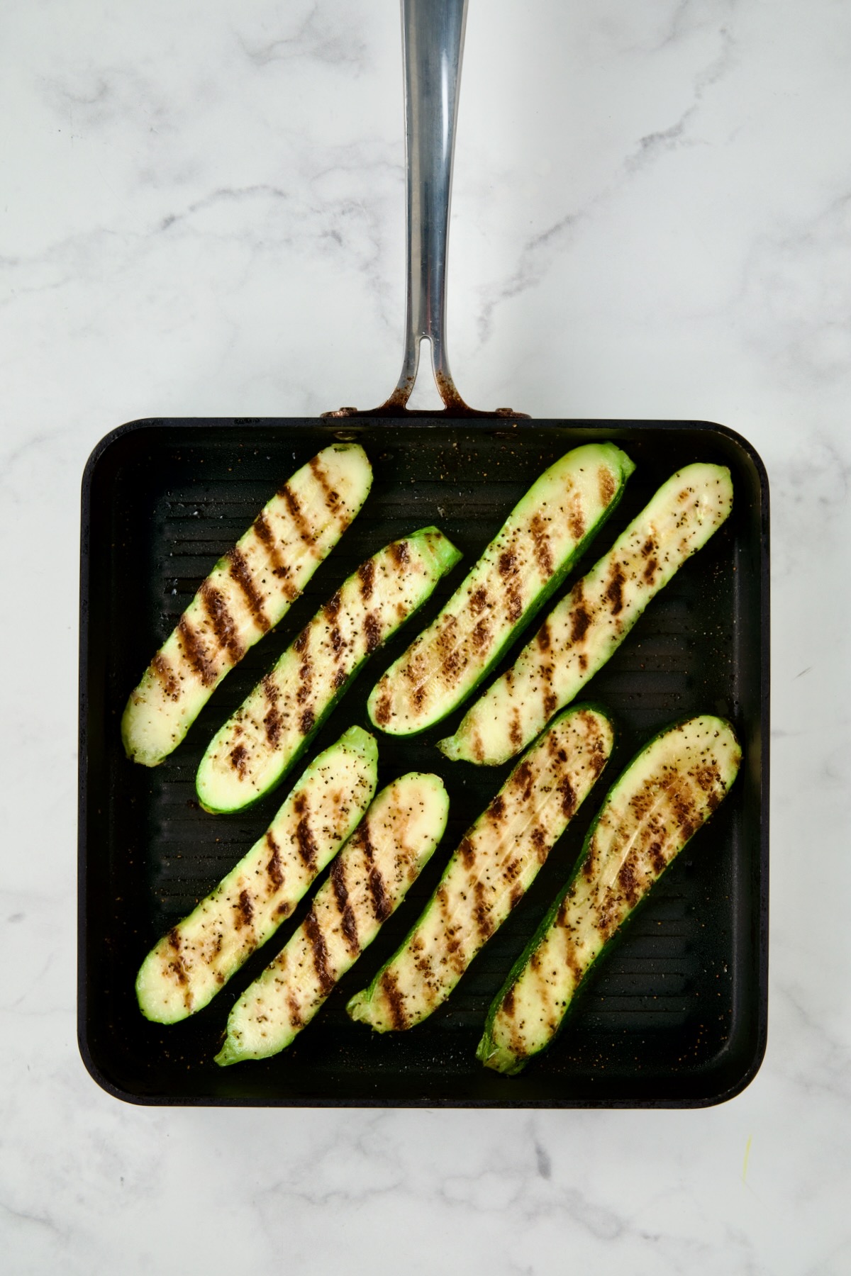 Eight grilled zucchini slices on square grill pan.