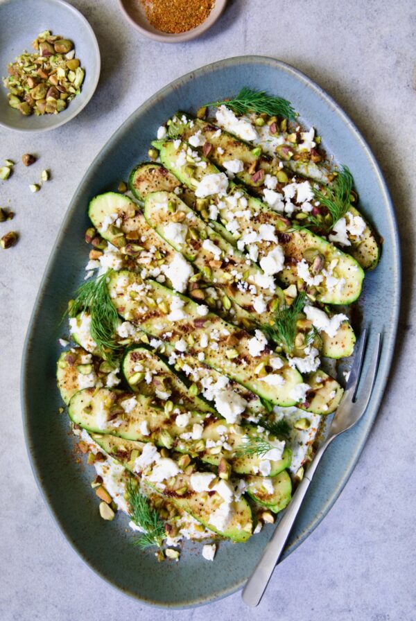 Mediterranean Grilled Zucchini with Dill Yogurt and Feta on blue platter garnished with pistachios and fresh dill sprigs.