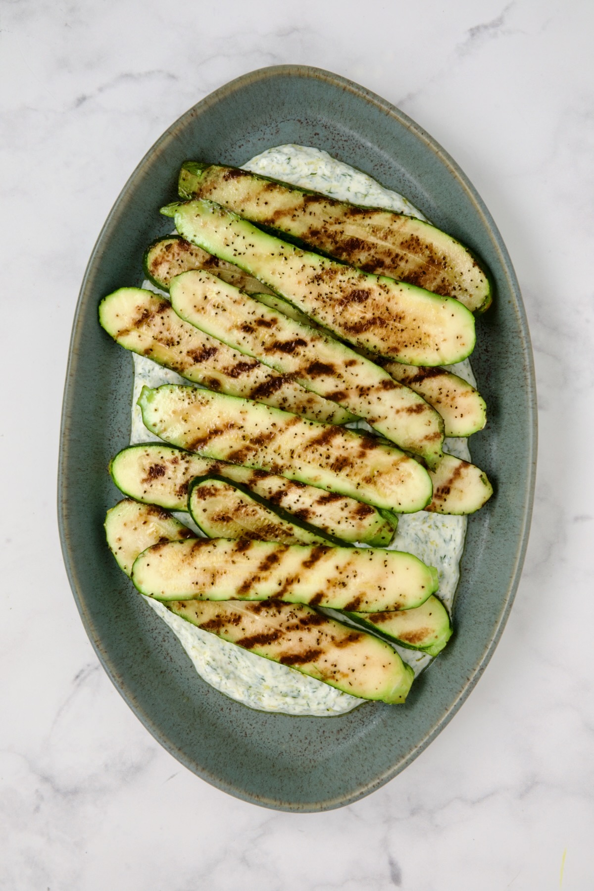 Grilled zucchini slices placed over dill yogurt on blue platter.
