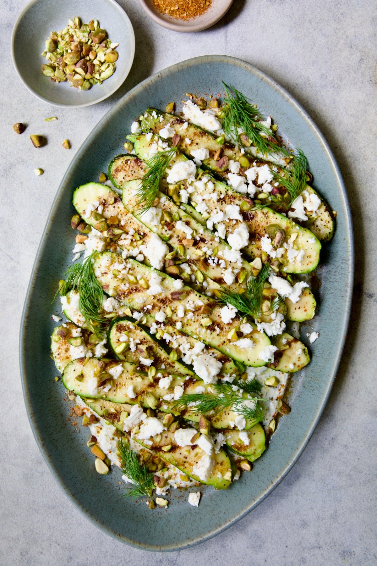 Mediterranean Grilled Zucchini with Dill Yogurt and Feta on blue platter garnished with pistachios and fresh dill sprigs.