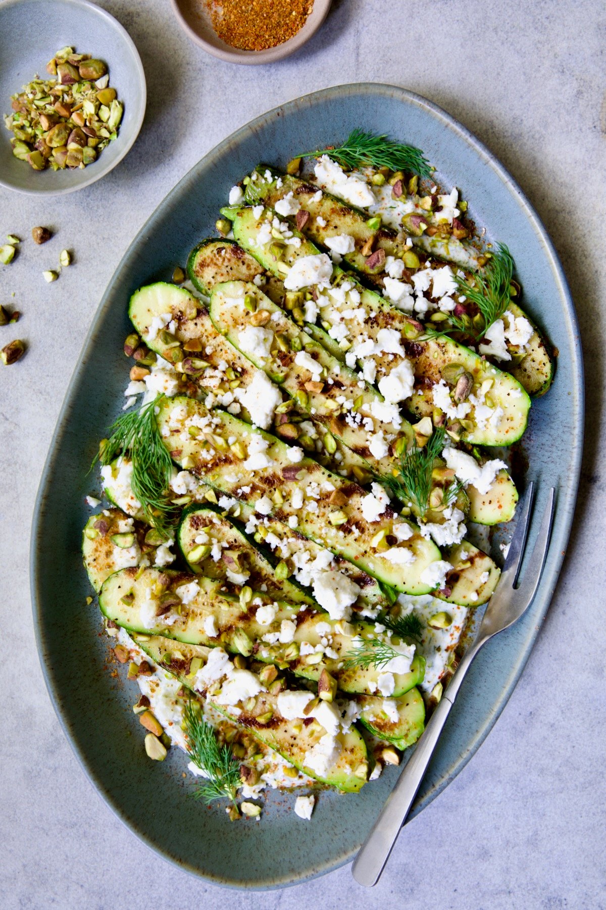 Mediterranean Grilled Zucchini with Dill Yogurt and Feta on blue platter garnished with pistachios and fresh dill sprigs.