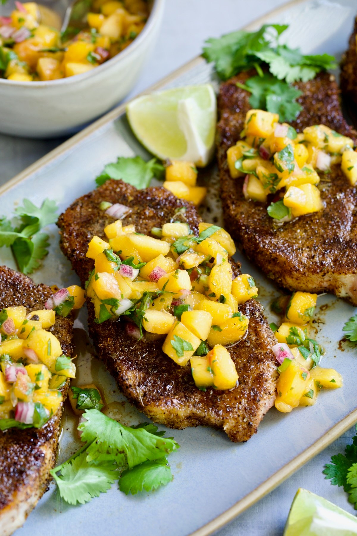 Three Pork Chops with Peach Salsa on oval gray platter.