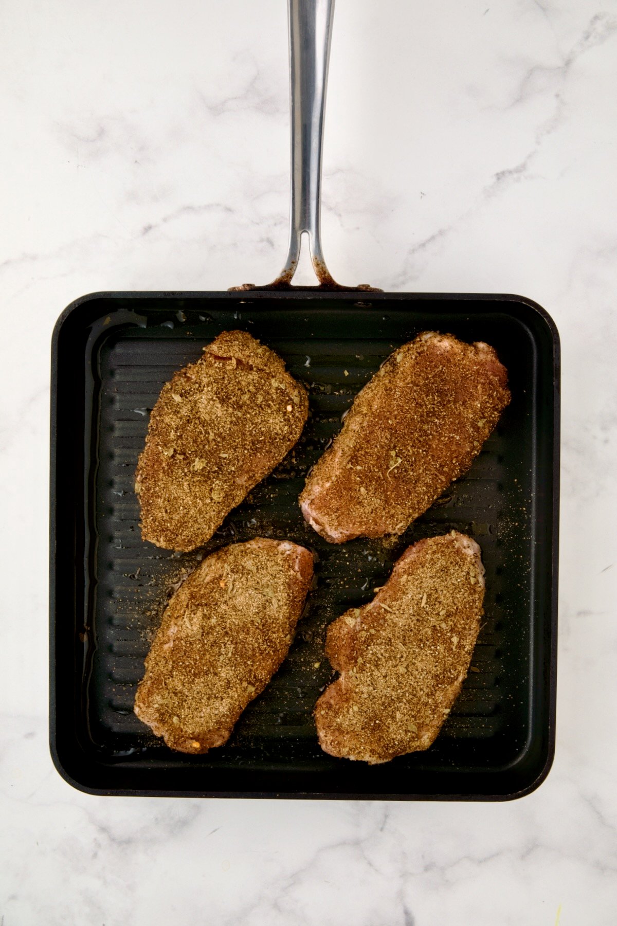 Four boneless pork chops rubbed with spice rub on square grill pan before being completely grilled.