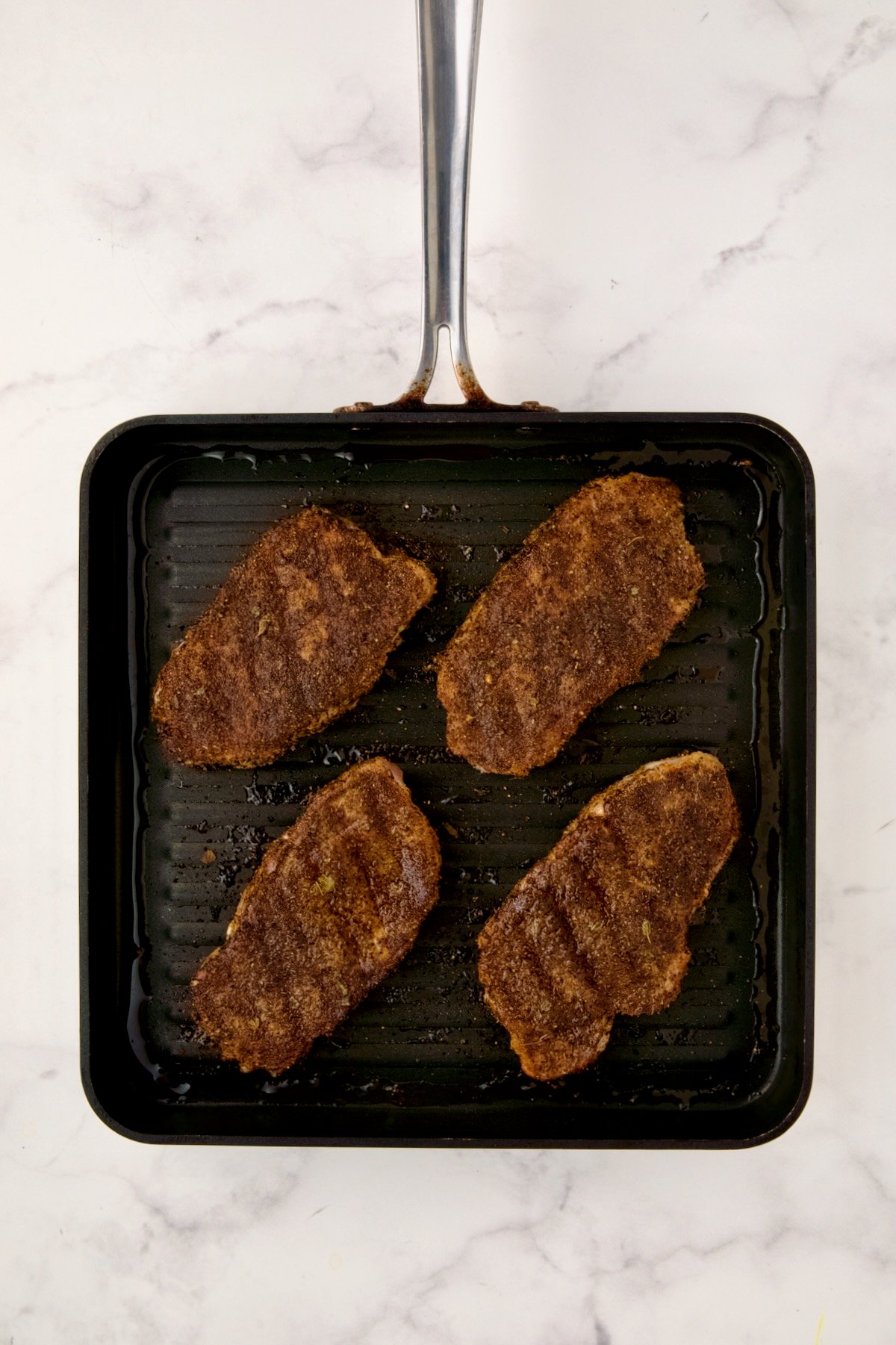 Four boneless pork on square grill pan after being completely grilled.
