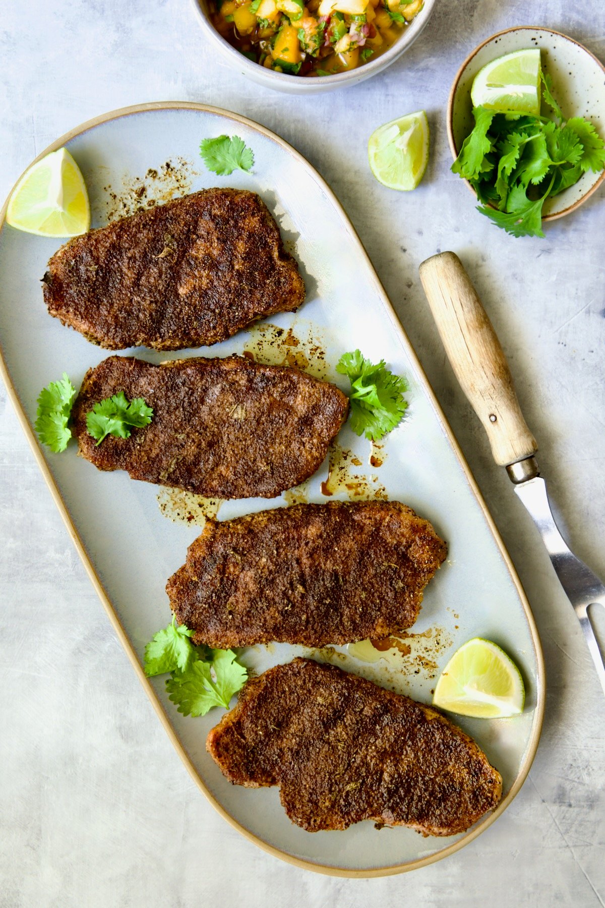 Four grilled boneless pork chops on gray oval platter before peach salsa is spooned over.